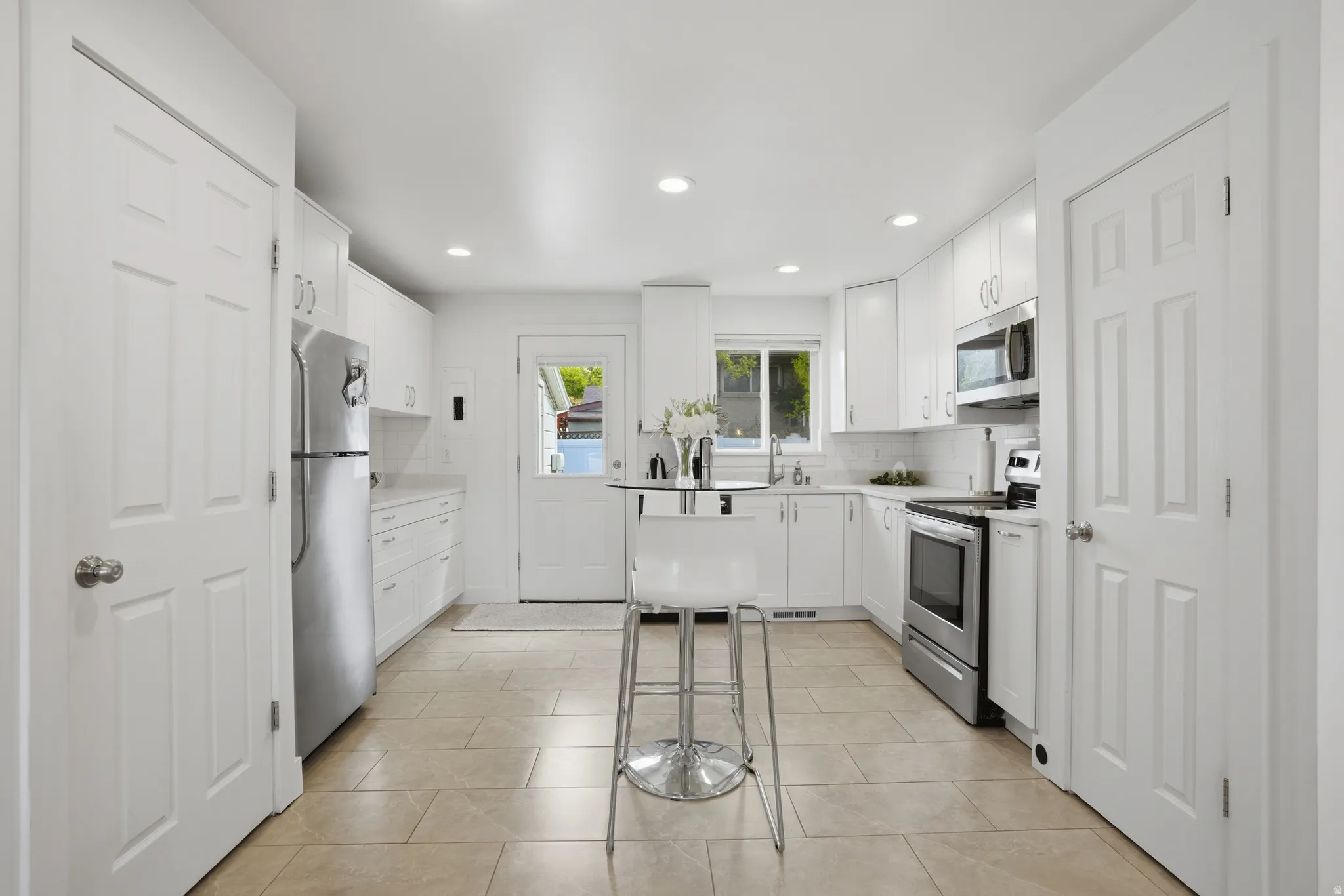 Kitchen featuring backsplash, white cabinetry, light countertops, stainless steel appliances, and recessed lighting