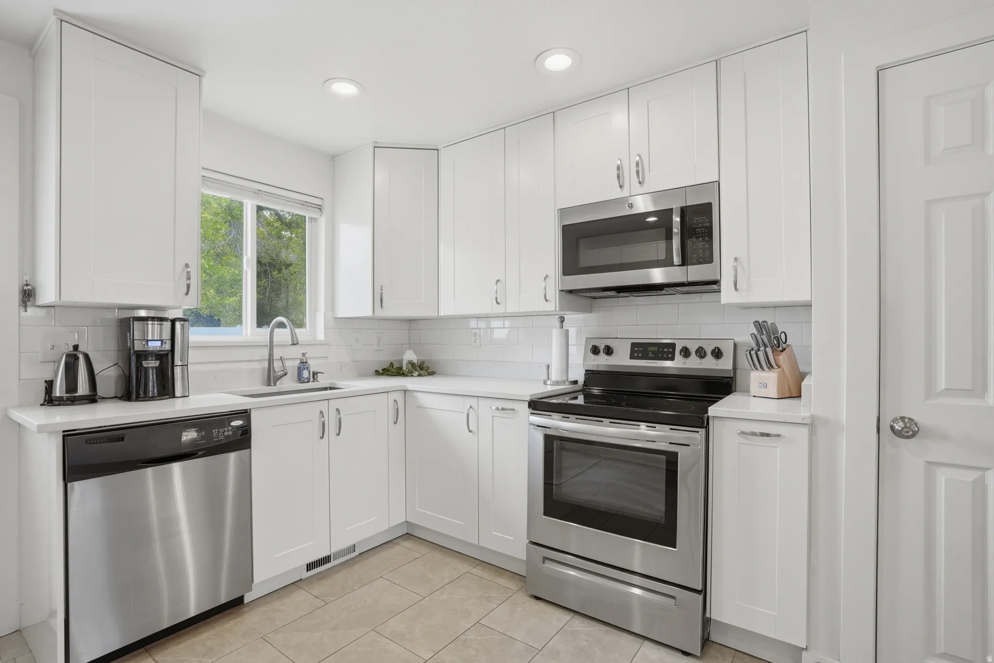 Kitchen with stainless steel appliances, white cabinets, light tile patterned floors, recessed lighting, and backsplash