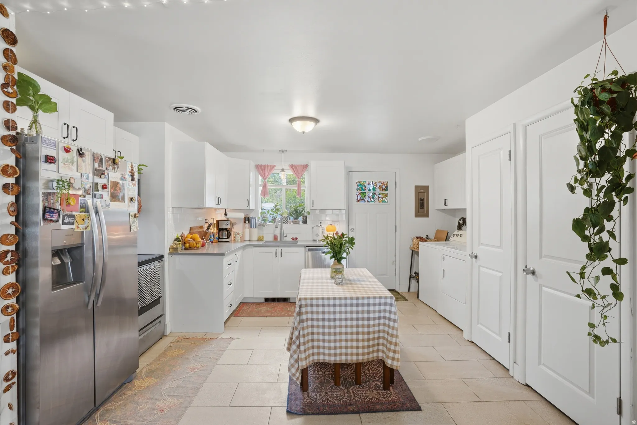 Kitchen featuring stainless steel appliances, decorative backsplash, white cabinets, and light tile patterned floors