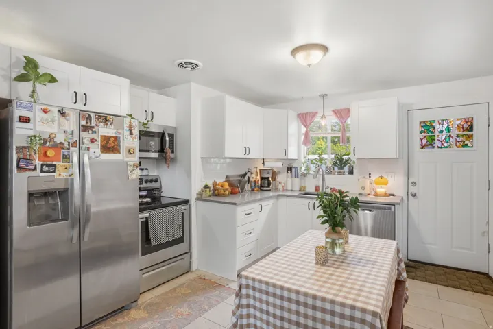 Kitchen with stainless steel appliances, white cabinetry, decorative light fixtures, and decorative backsplash