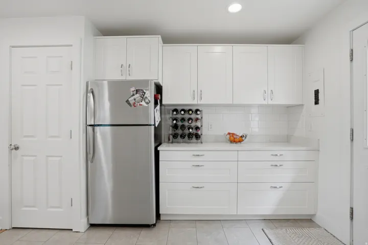 Kitchen featuring freestanding refrigerator, white cabinets, decorative backsplash, recessed lighting, and electric panel