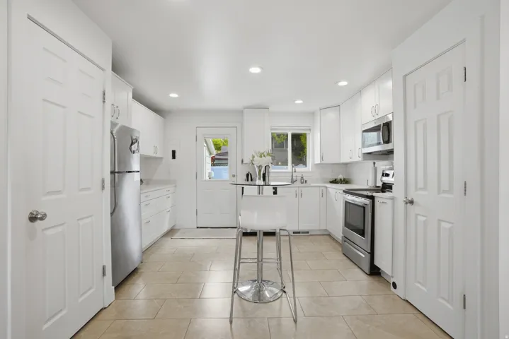 Kitchen featuring backsplash, white cabinetry, light countertops, stainless steel appliances, and recessed lighting