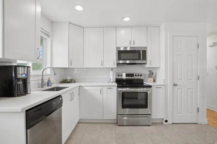 Kitchen with stainless steel appliances, white cabinets, light stone counters, backsplash, and recessed lighting