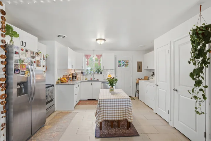 Kitchen featuring stainless steel appliances, decorative backsplash, white cabinets, and light tile patterned floors