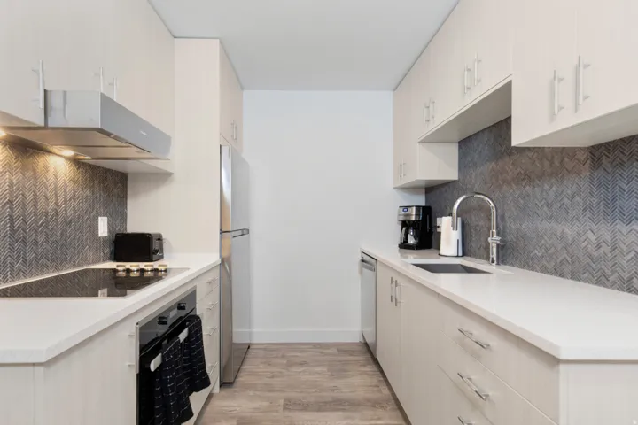 Kitchen featuring light wood-style floors, oven, light stone counters, backsplash, and freestanding refrigerator