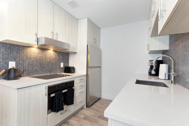 Kitchen with oven, light stone counters, freestanding refrigerator, light wood-type flooring, and tasteful backsplash