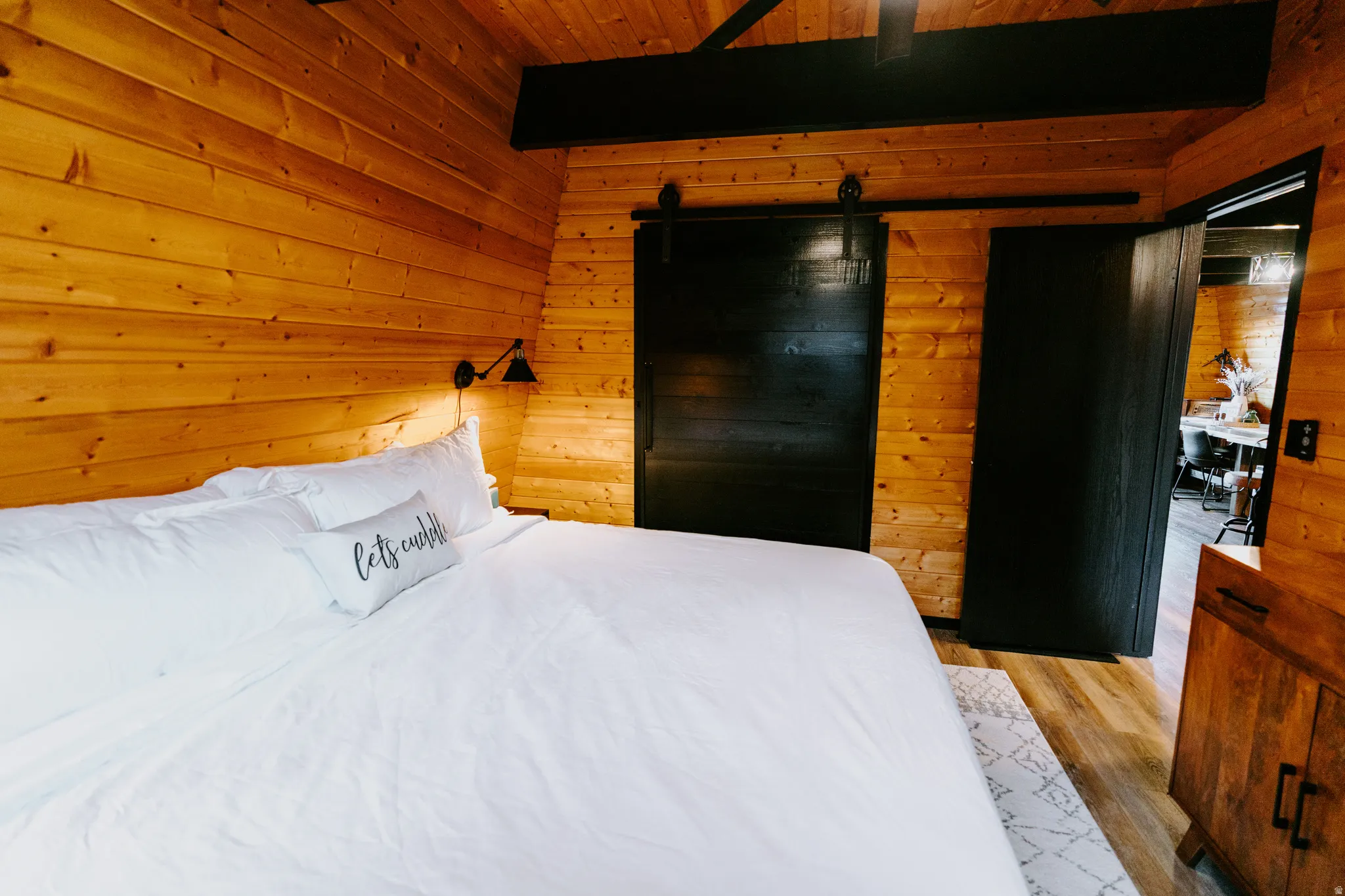 Bedroom with wood walls, ceiling fan, light wood-type flooring, a barn door, and a wood ceiling with exposed beams