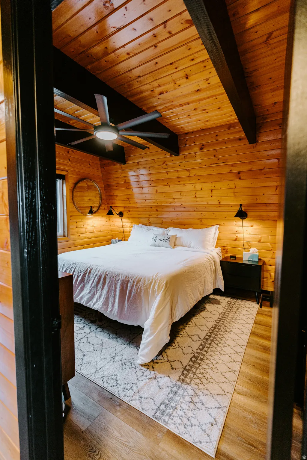 Bedroom with wooden walls, a wooden ceiling with exposed beams, light wood finished floors, and ceiling fan