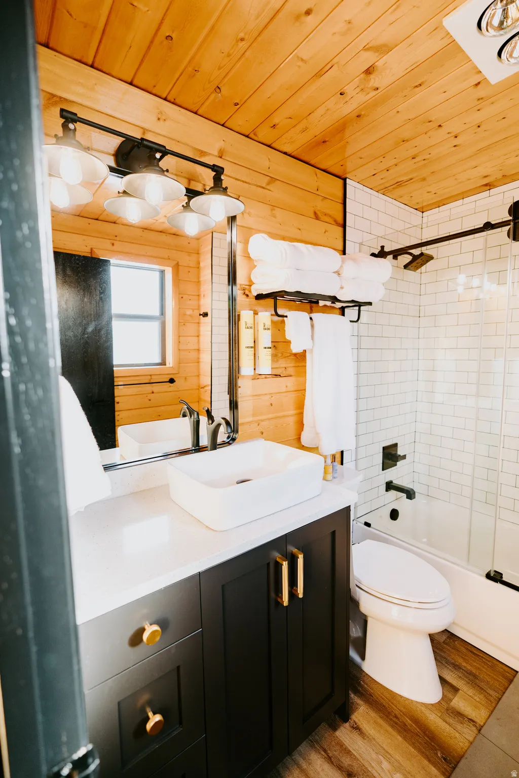 Bathroom with wooden ceiling, vanity, wooden walls, light wood finished floors, and shower / washtub combination