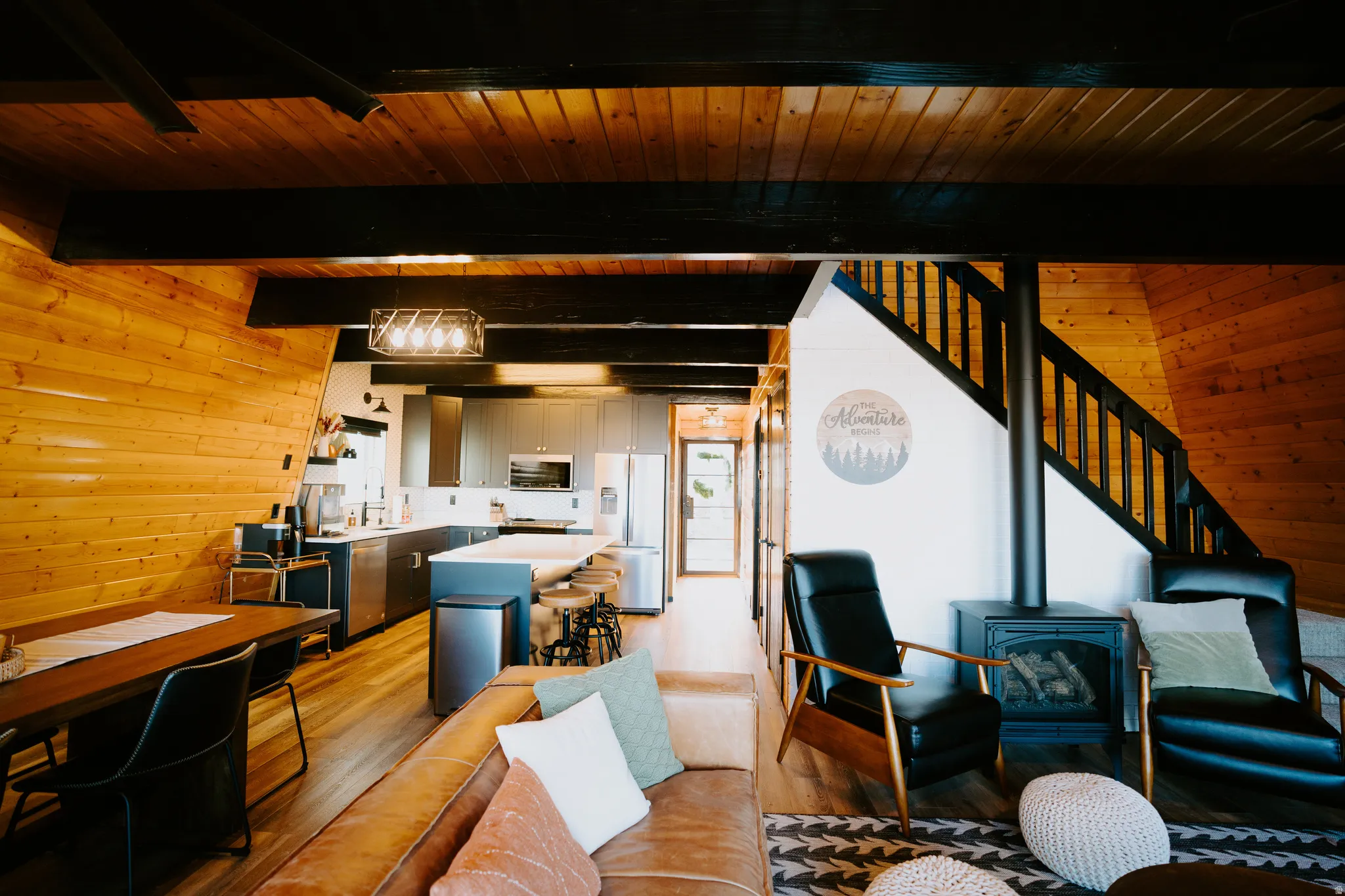 Living area with wooden walls, a wood stove, light wood-type flooring, and a wood ceiling with exposed beams