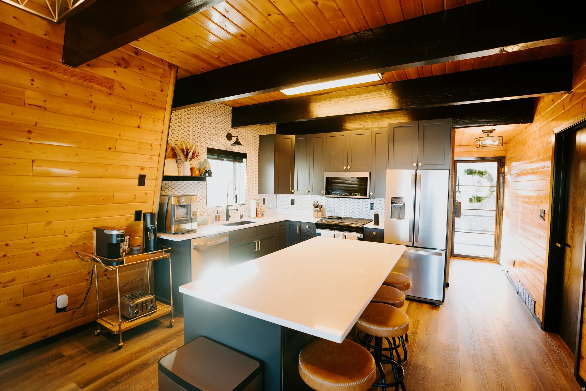 Kitchen with stainless steel appliances, light wood-style flooring, wood walls, a kitchen island, and a wooden ceiling with exposed beams