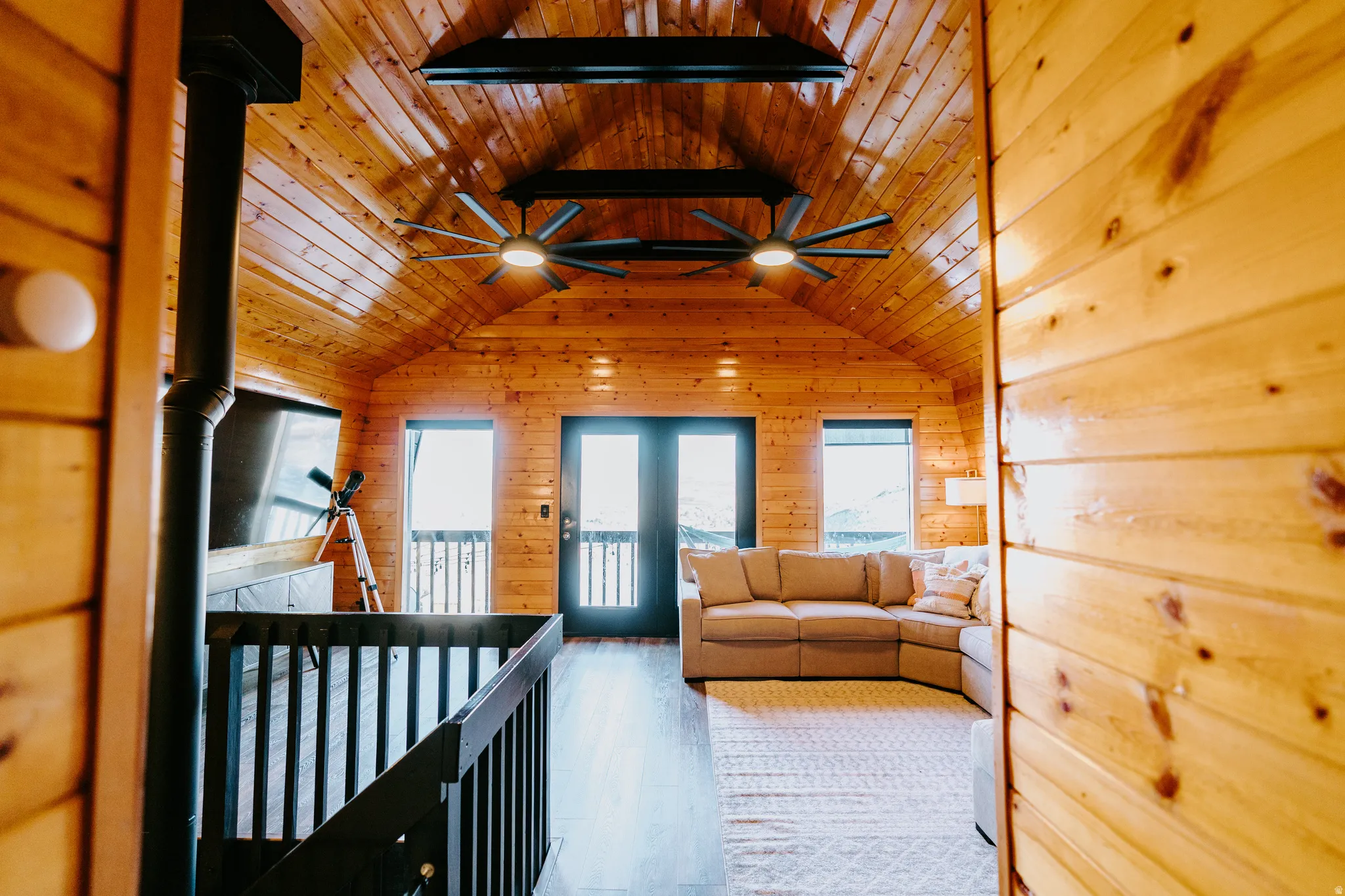 Living area with ceiling fan, light wood-style floors, wood walls, a wood ceiling with exposed beams, and a wood stove