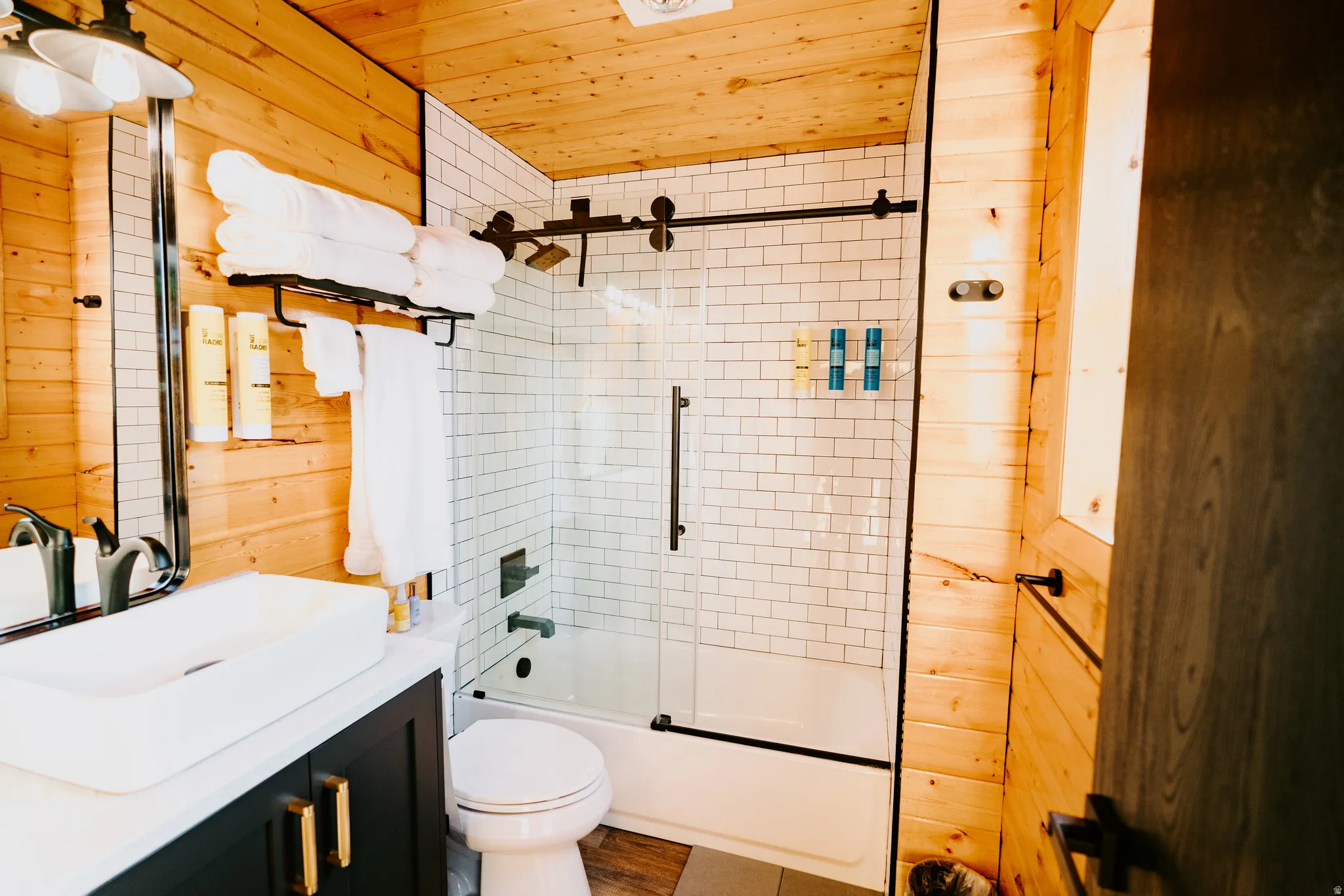 Bathroom with wooden walls, bath / shower combo with glass door, vanity, and wooden ceiling