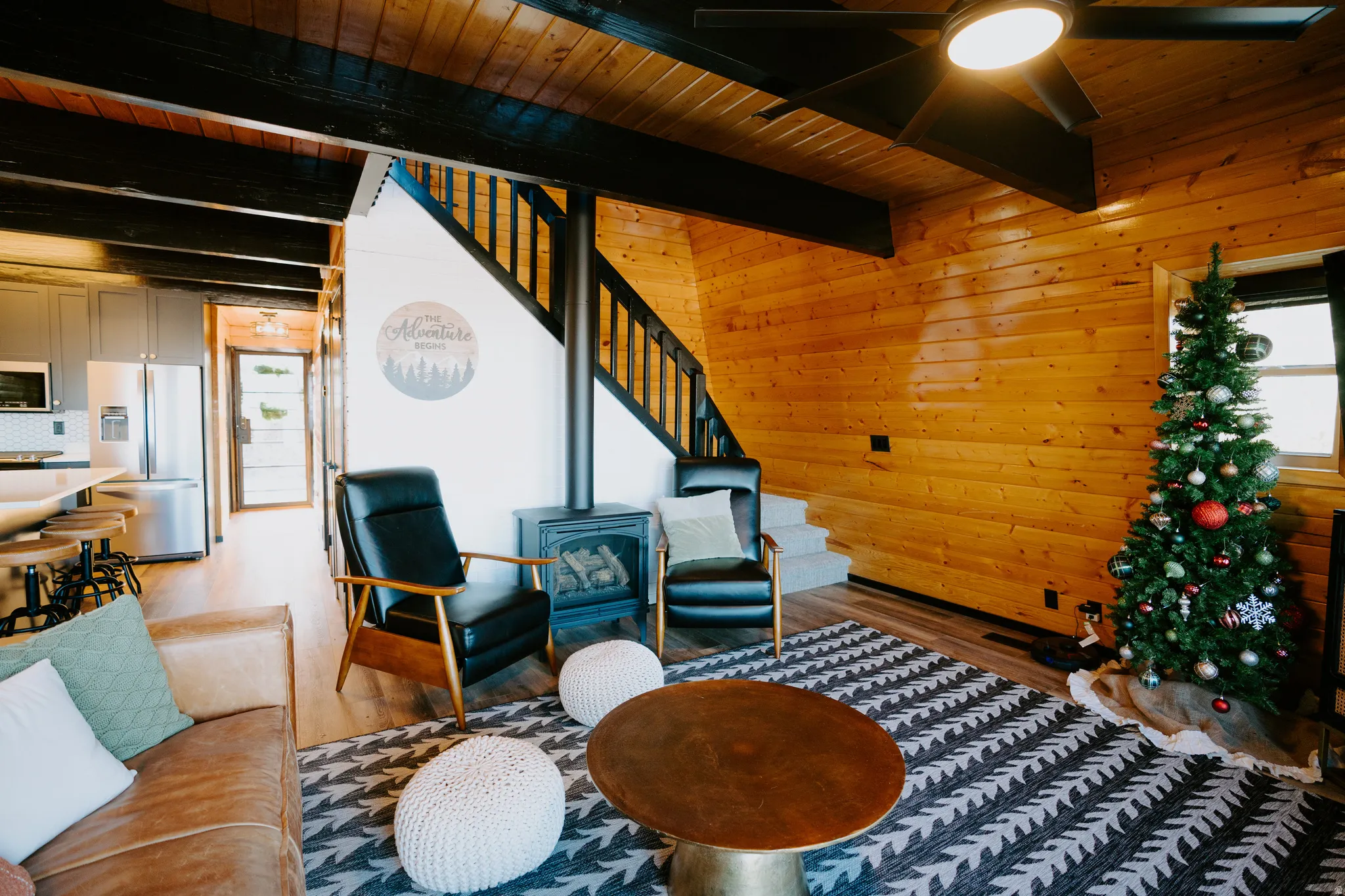 Living area with wood walls, a wood stove, wood finished floors, a wooden ceiling with exposed beams, and ceiling fan