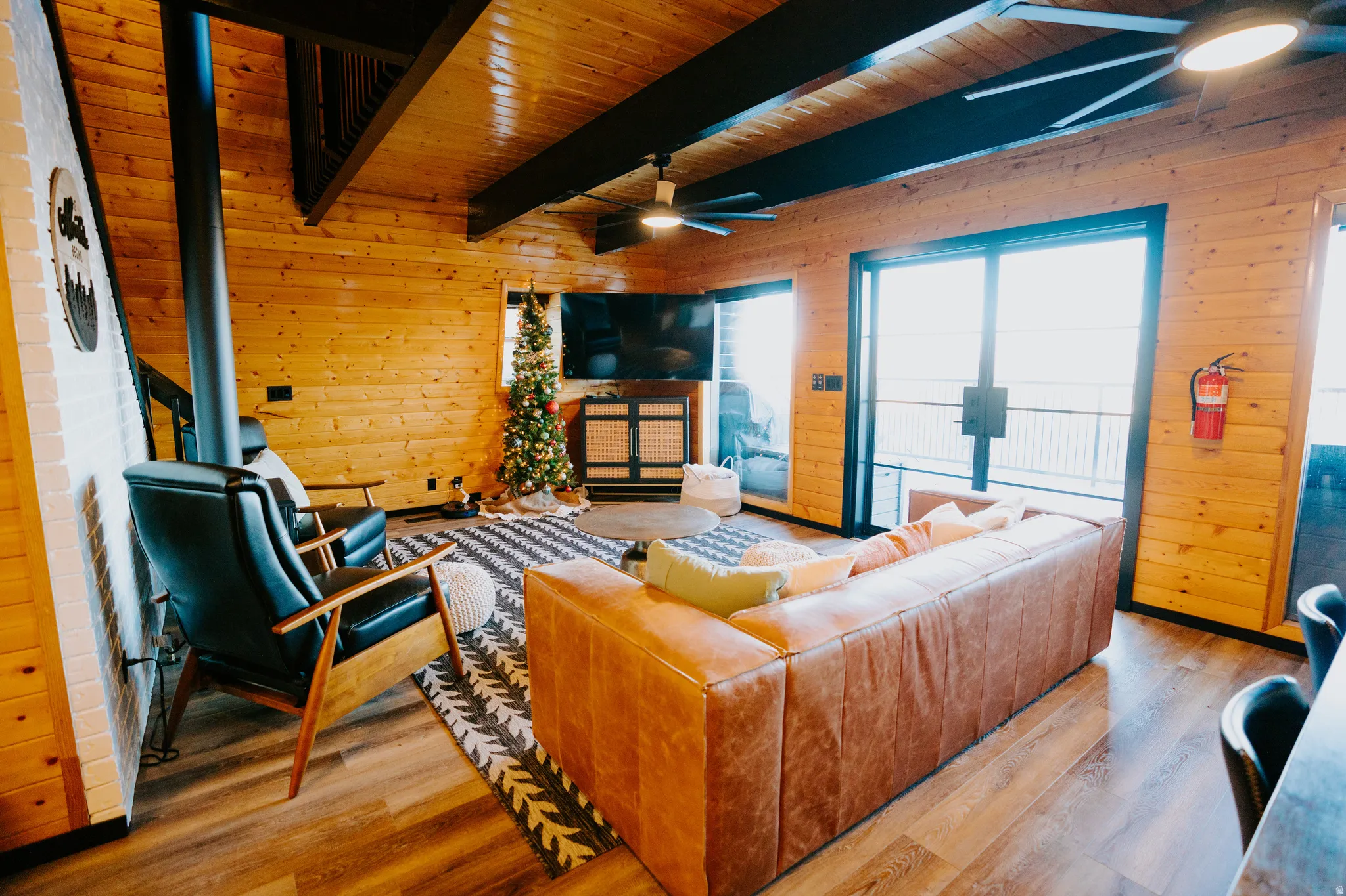 Living area featuring wood walls, a ceiling fan, wood finished floors, and a wooden ceiling with exposed beams