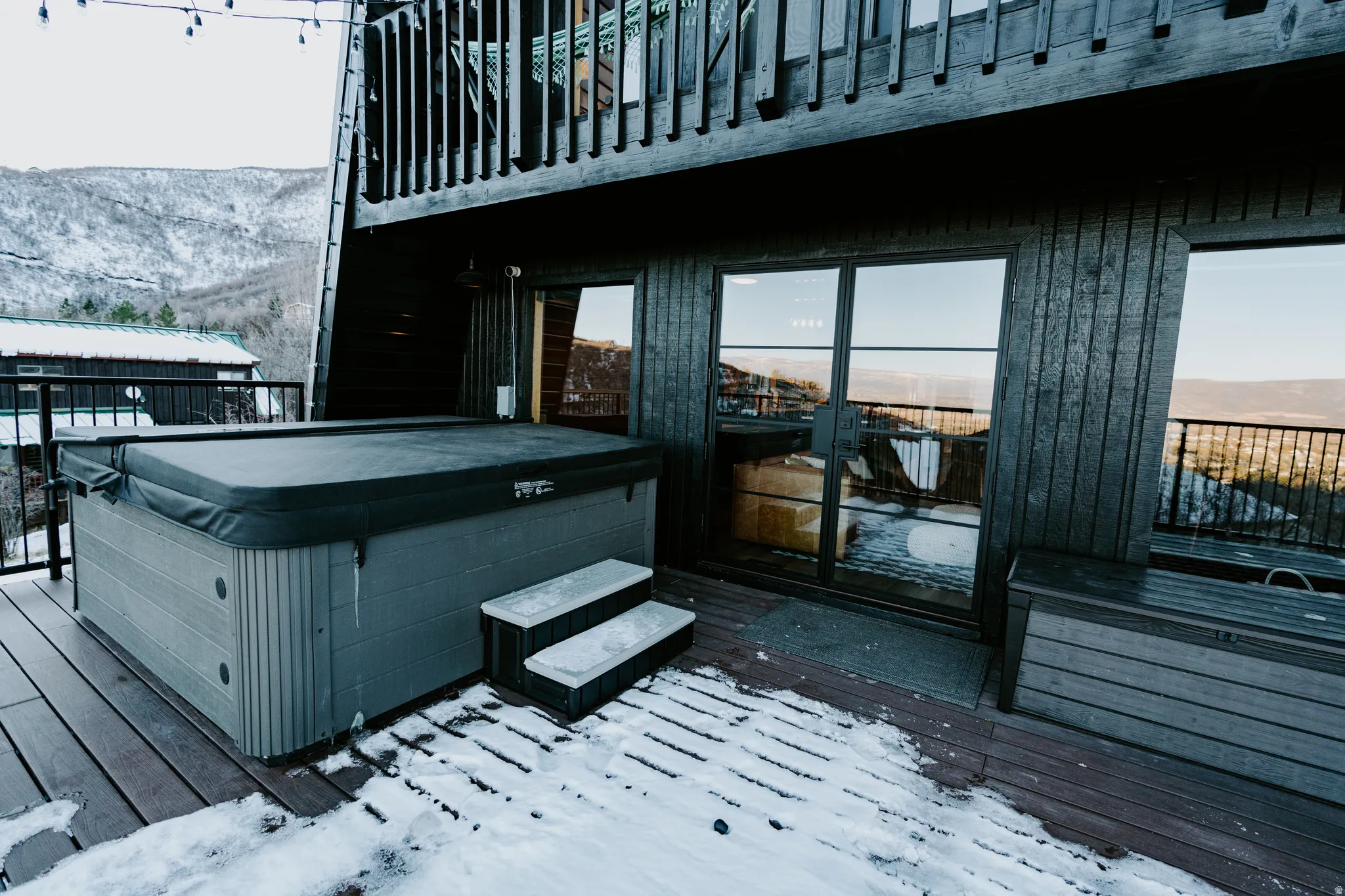 Snow covered deck featuring a mountain view and a hot tub