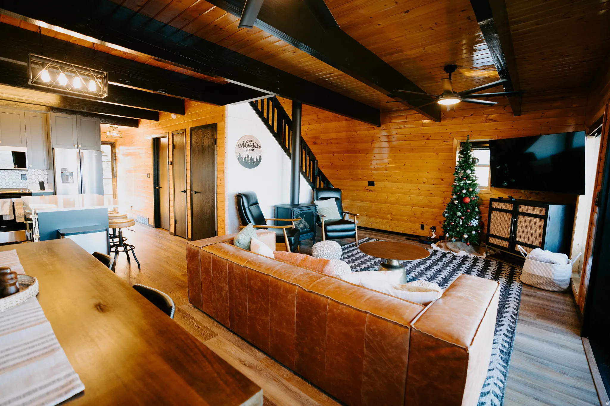 Living room featuring wood walls, light wood-style floors, a wooden ceiling with exposed beams, and ceiling fan