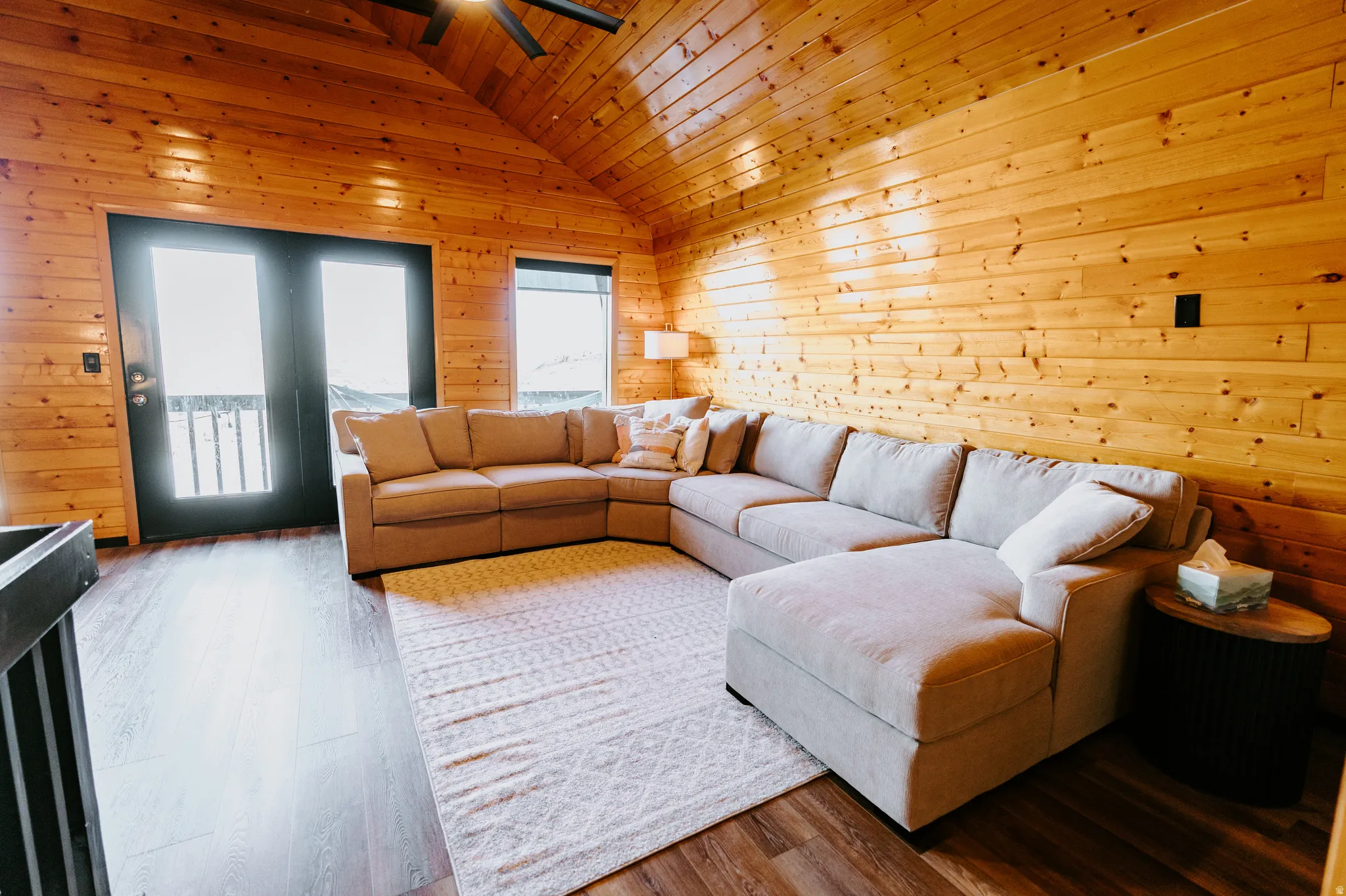 Living room featuring wood walls, wood finished floors, a ceiling fan, and a vaulted wooden ceiling