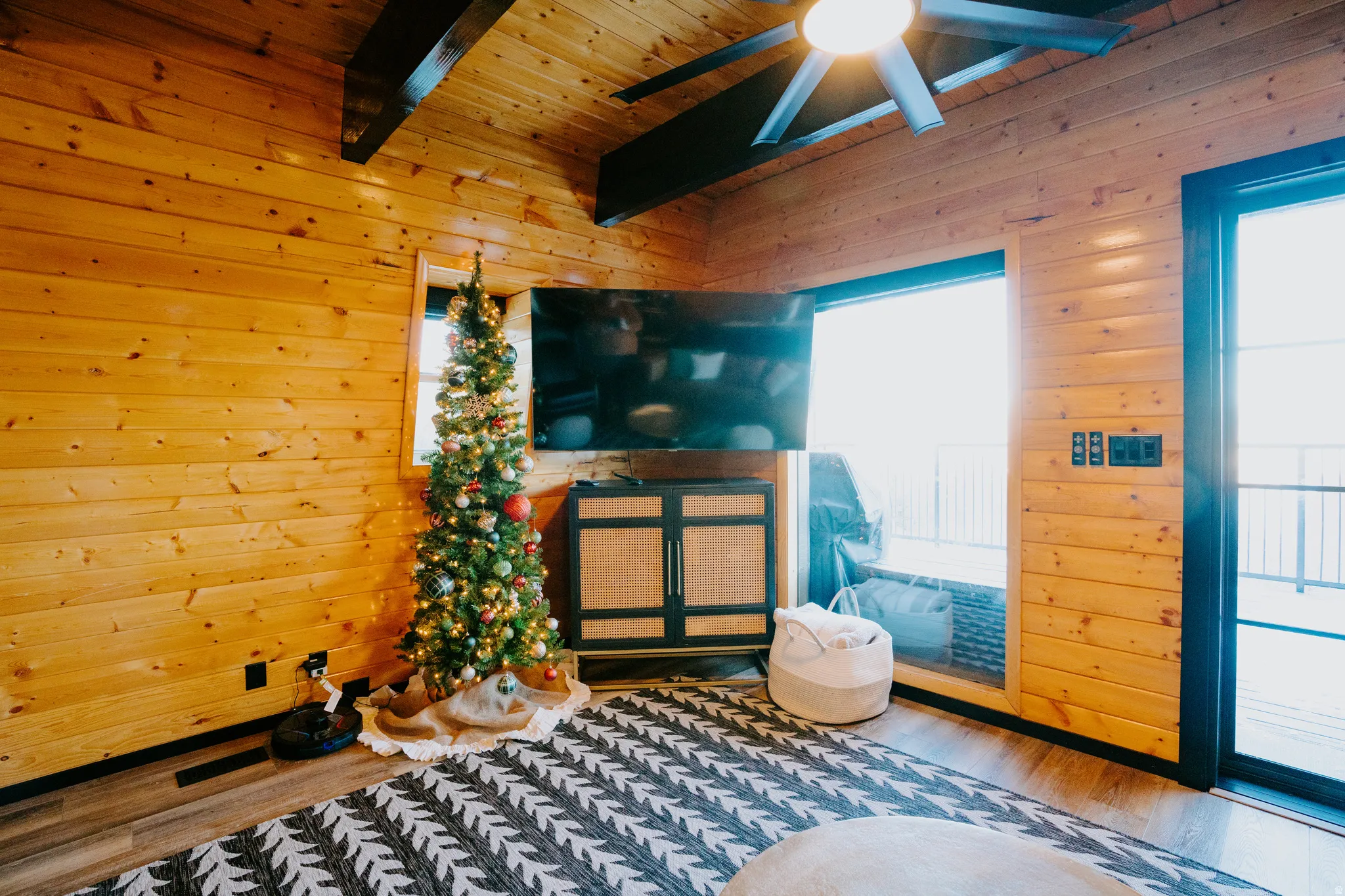 Sitting room with wooden walls, wood finished floors, ceiling fan, and a wooden ceiling with exposed beams