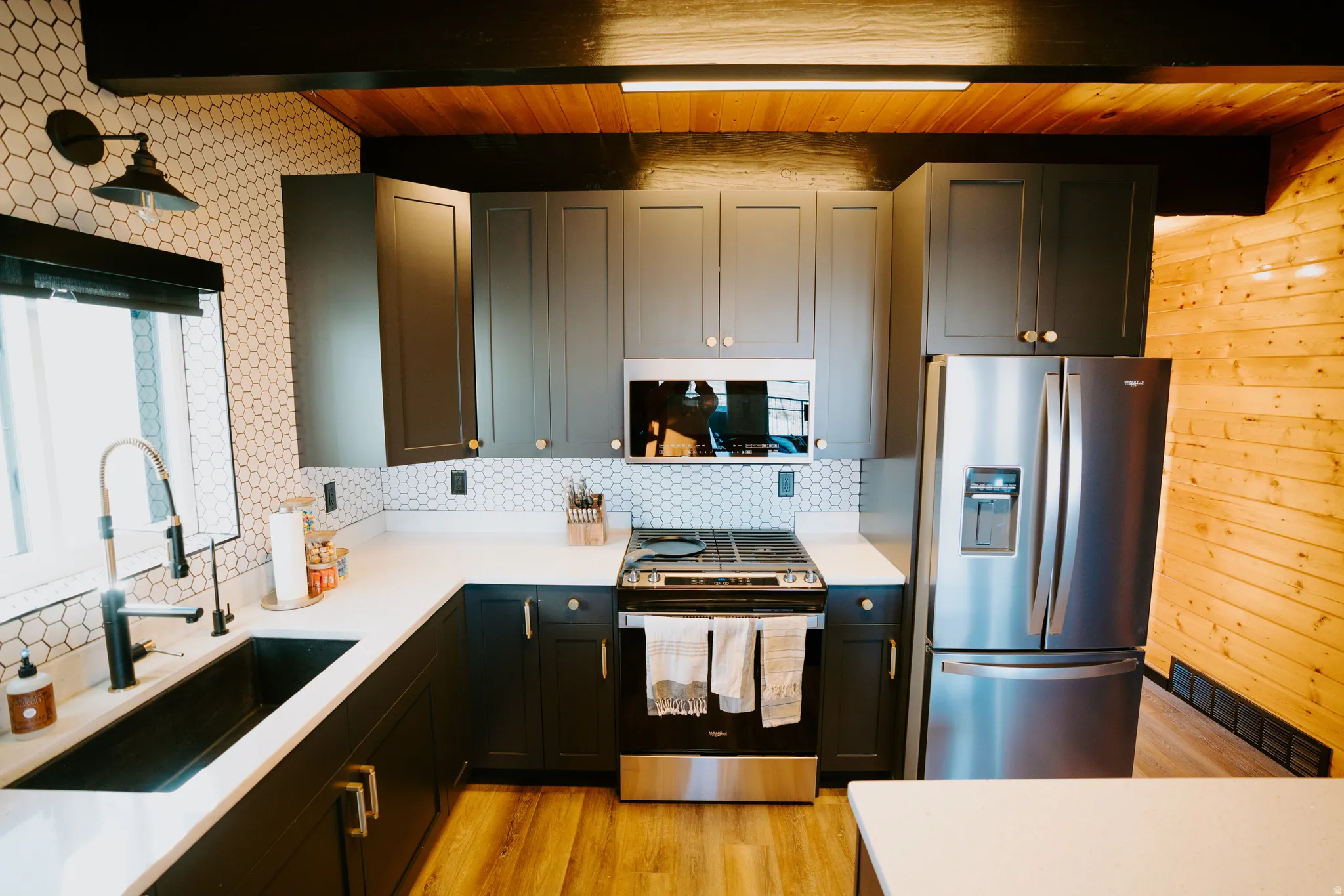 Kitchen featuring stainless steel appliances, light wood-style floors, decorative backsplash, light stone countertops, and beam ceiling