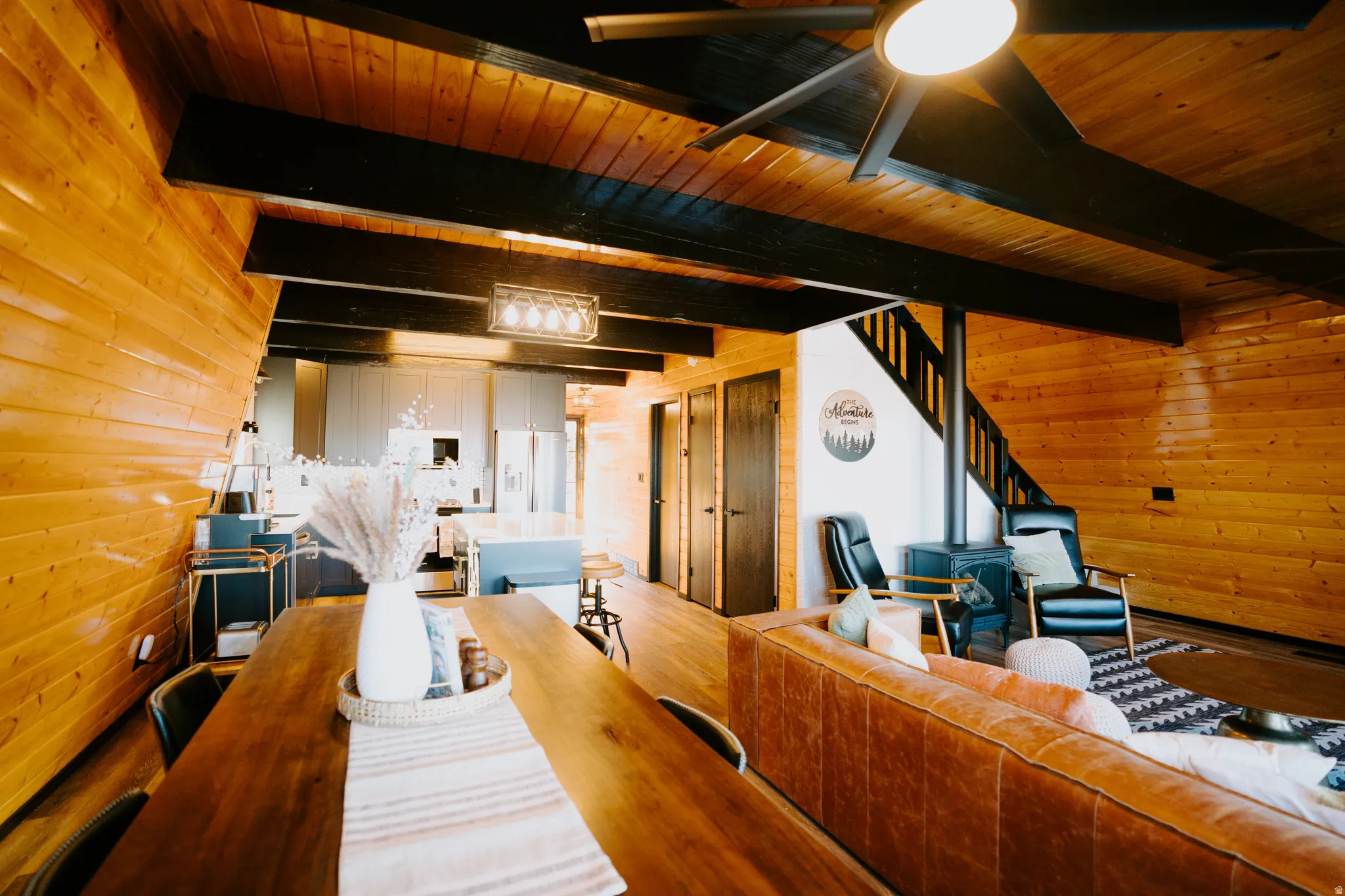 Living room with wooden walls, ceiling fan, wood finished floors, and a wood ceiling with exposed beams