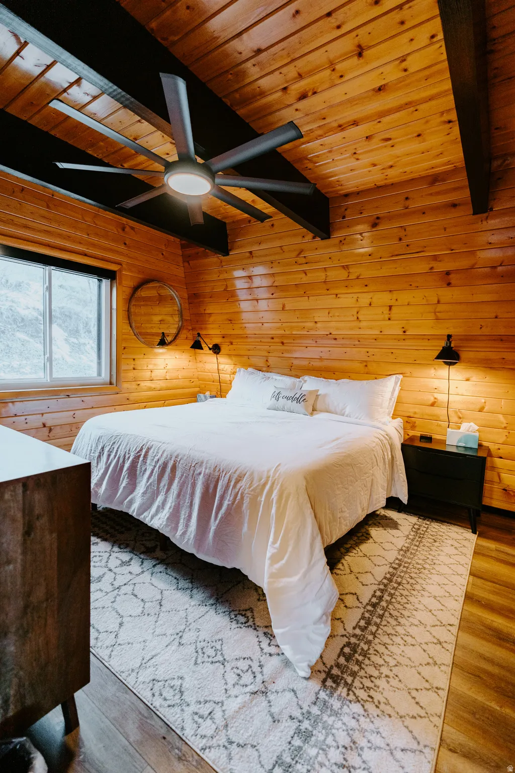 Bedroom with a wooden ceiling with exposed beams, wood walls, a ceiling fan, and wood finished floors