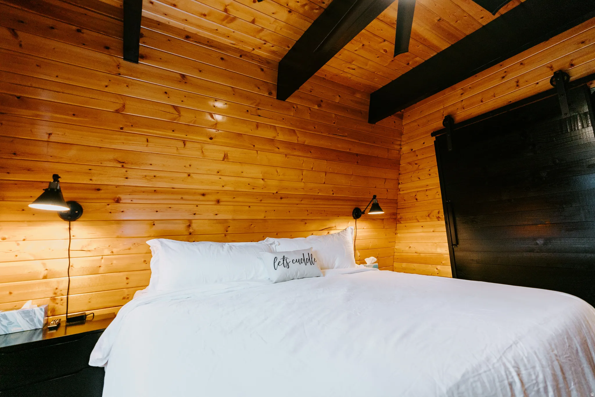 Bedroom featuring wood walls, a wooden ceiling with exposed beams, and a barn door