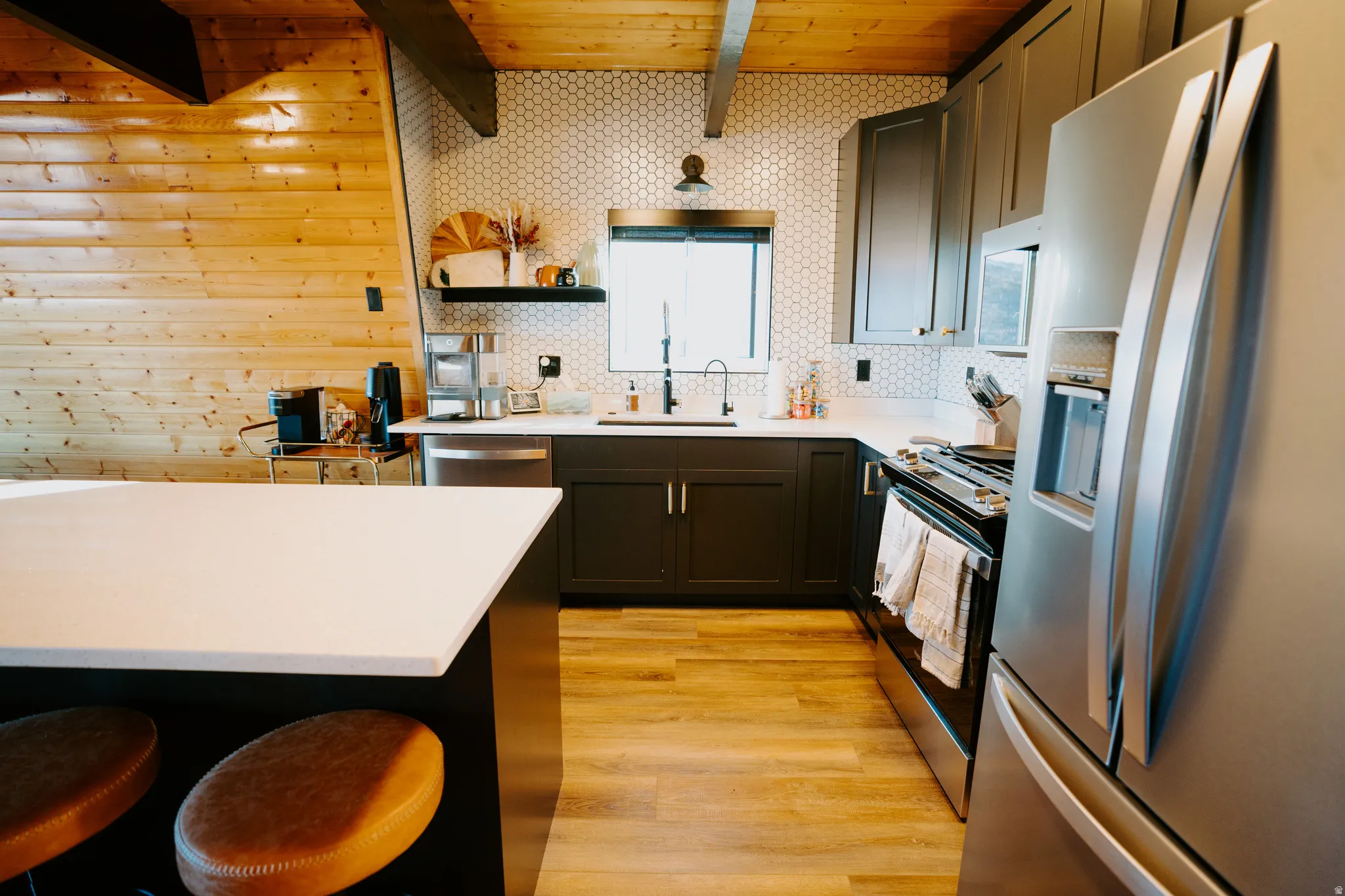 Kitchen with stainless steel appliances, a breakfast bar, light wood-type flooring, open shelves, and a wooden ceiling with exposed beams