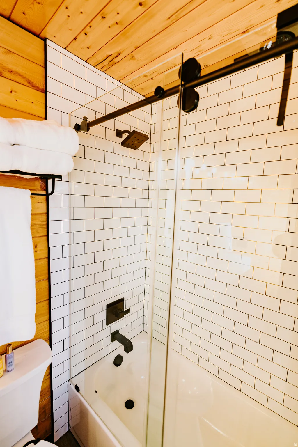 Full bath with wooden ceiling, enclosed tub / shower combo, and wooden walls