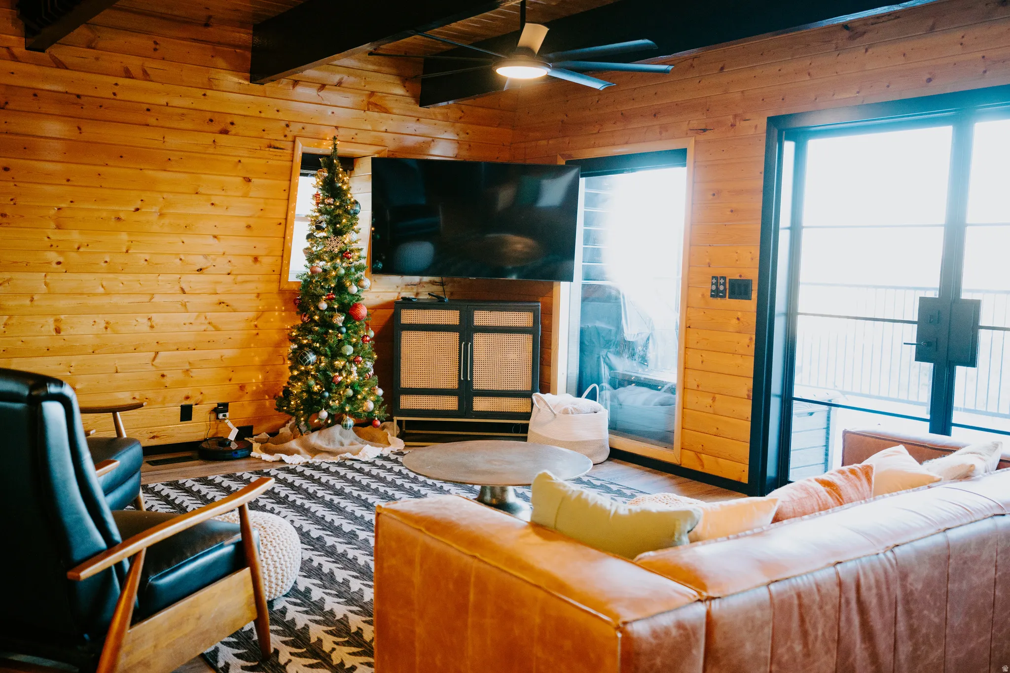 Living room with wood walls, ceiling fan, wood finished floors, and a wood ceiling with exposed beams
