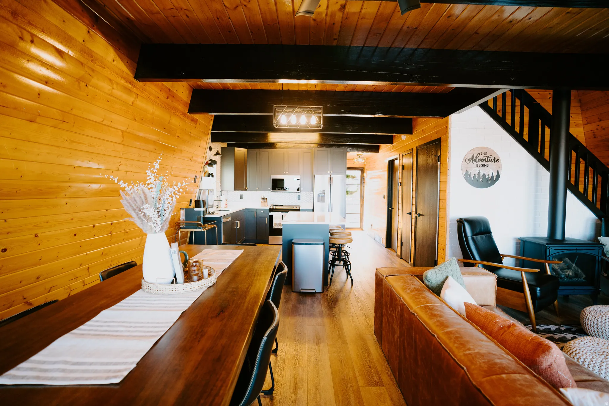 Living area featuring a wood stove, wooden walls, light wood-style floors, and a wooden ceiling with exposed beams