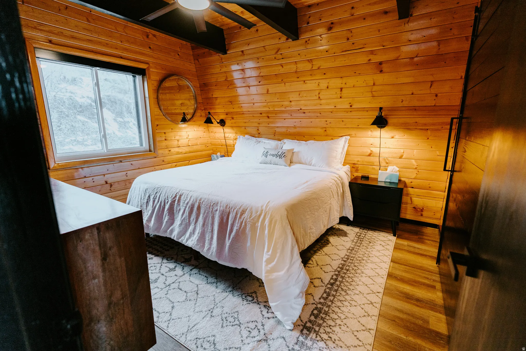 Bedroom with wooden walls, light wood-type flooring, beamed ceiling, and ceiling fan