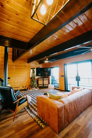 Living area featuring wooden walls, a wood ceiling with exposed beams, wood finished floors, ceiling fan, and a wood stove