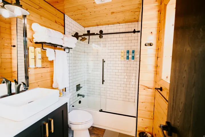 Bathroom with wooden walls, bath / shower combo with glass door, vanity, and wooden ceiling