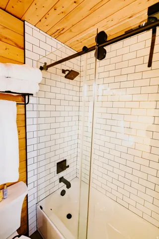 Full bath with wooden ceiling, enclosed tub / shower combo, and wooden walls