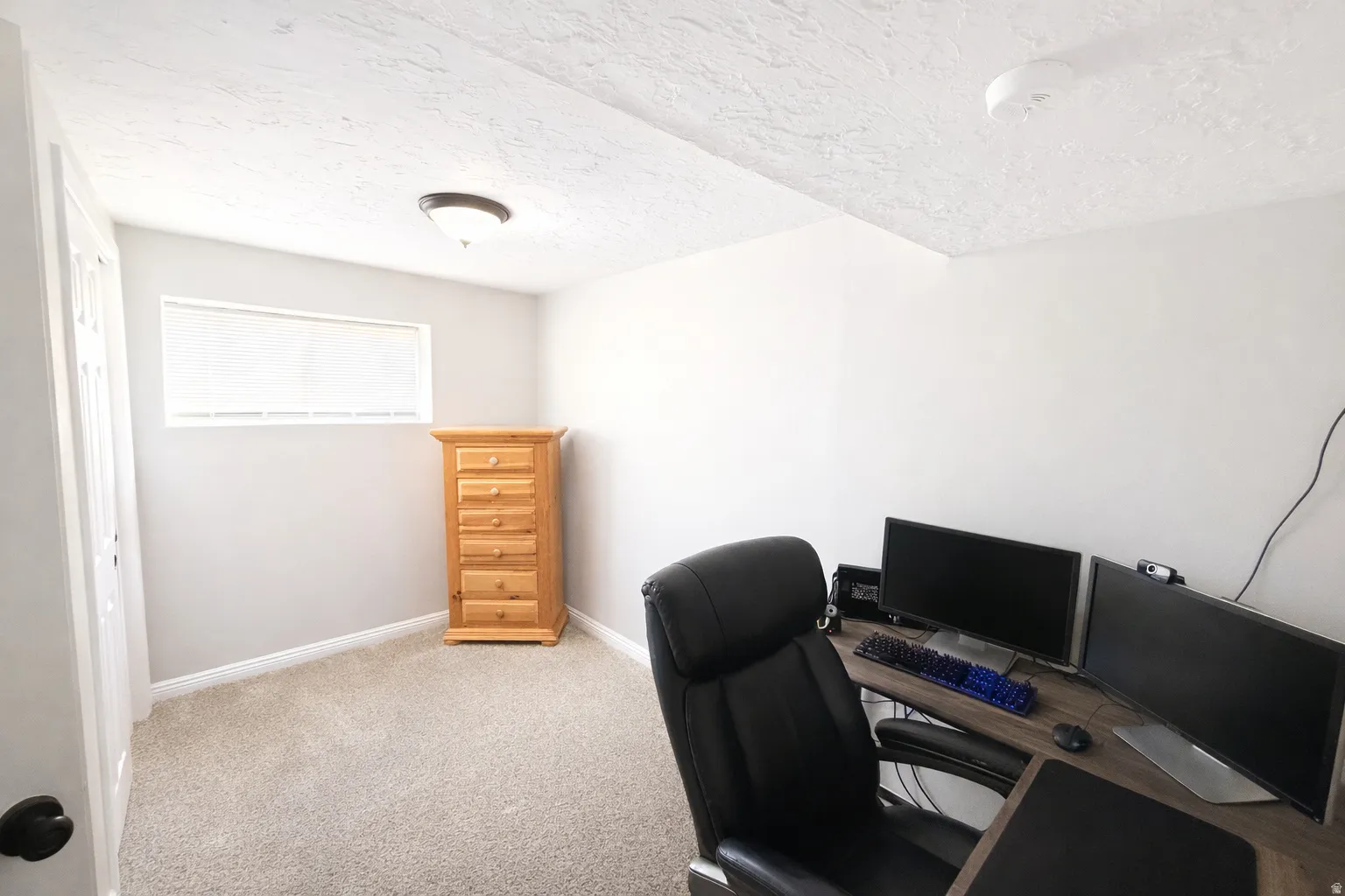 Carpeted office/bedroom space with baseboards and a textured ceiling