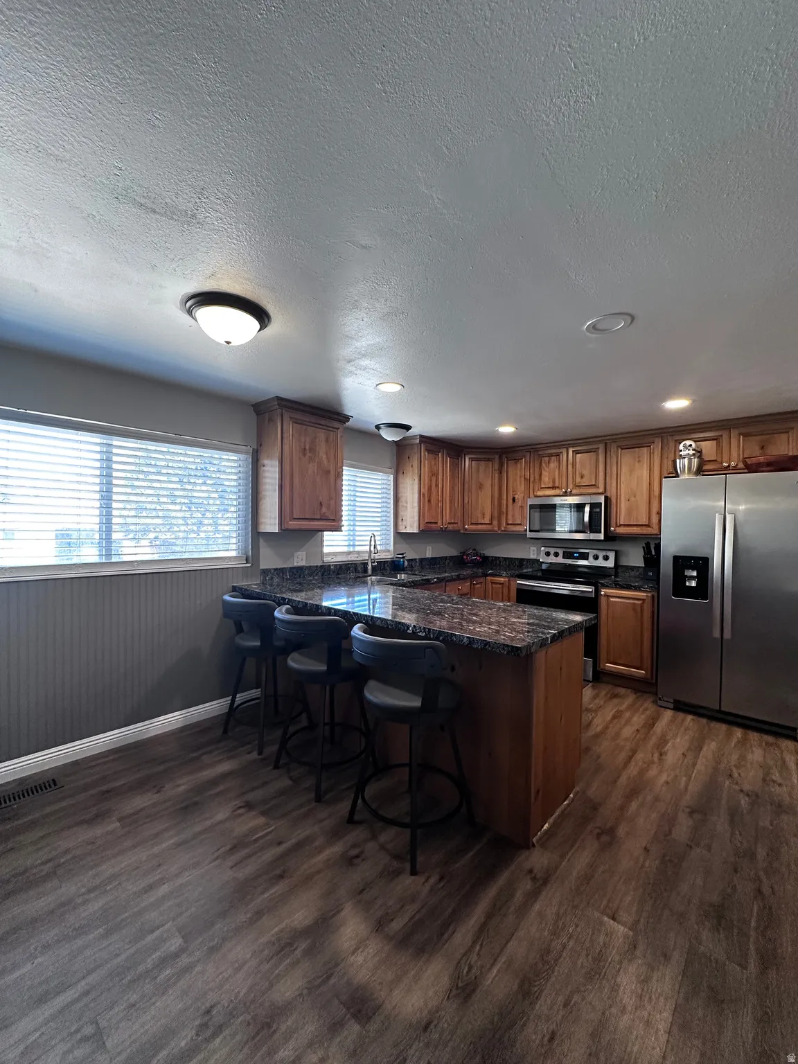 Kitchen with stainless steel stove, wood finish cabinets, dark stone countertops, dark wood finished floors, and a textured ceiling