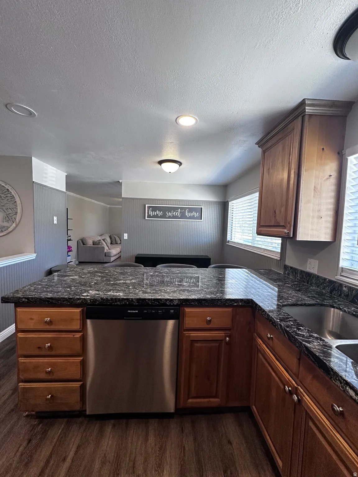 Kitchen featuring stainless steel dishwasher, a peninsula, dark wood-type flooring, open floor plan, and a textured ceiling
