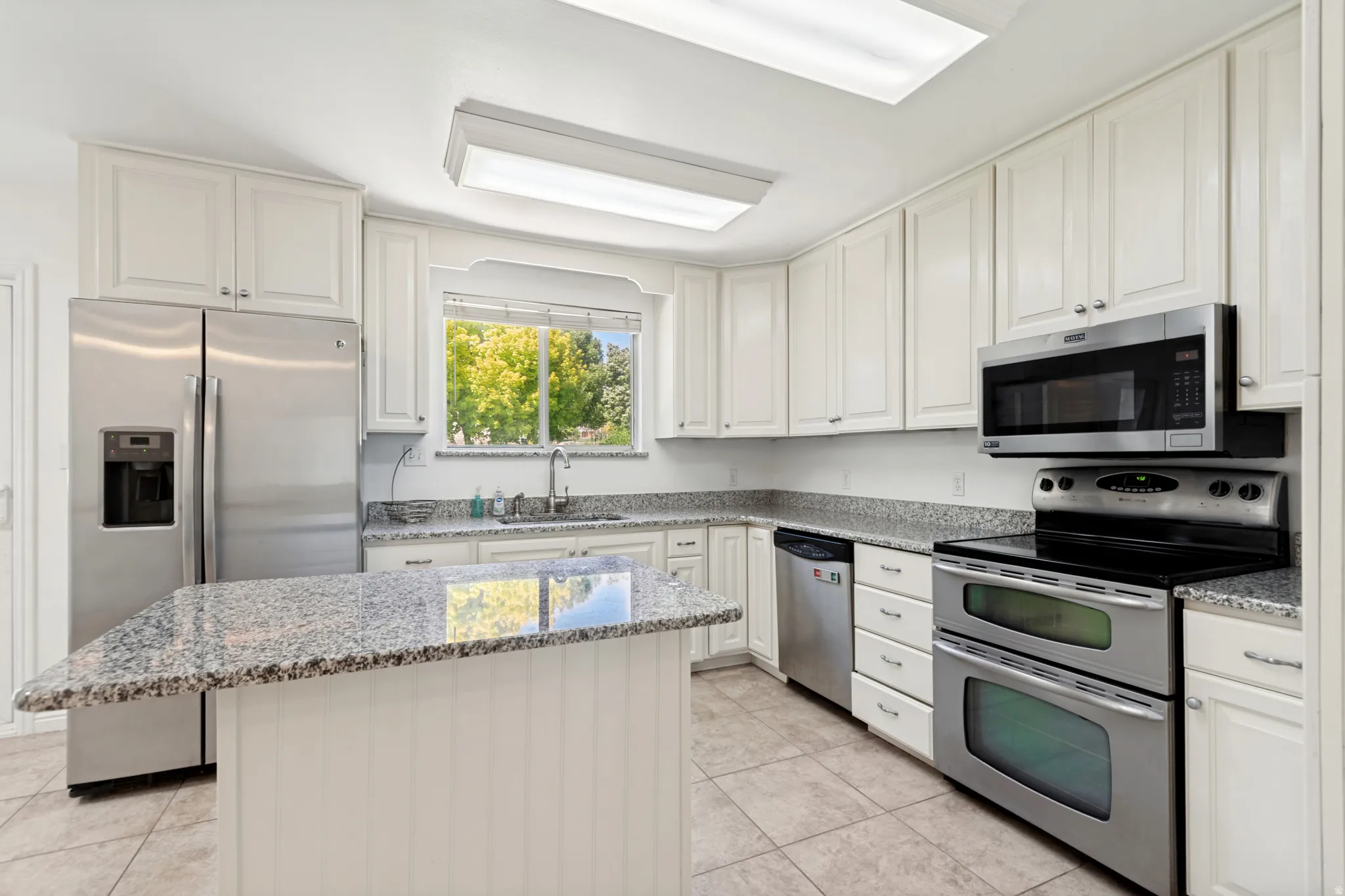 Kitchen featuring white cabinetry, granite countertops, stainless steel appliances, a center island with beadboard paneling, and tile flooring