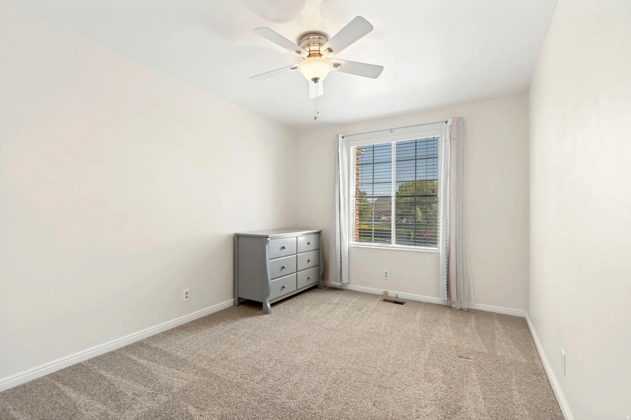 Neutral-toned room featuring a window with horizontal blinds, a ceiling fan with integrated lighting, and plush carpet flooring