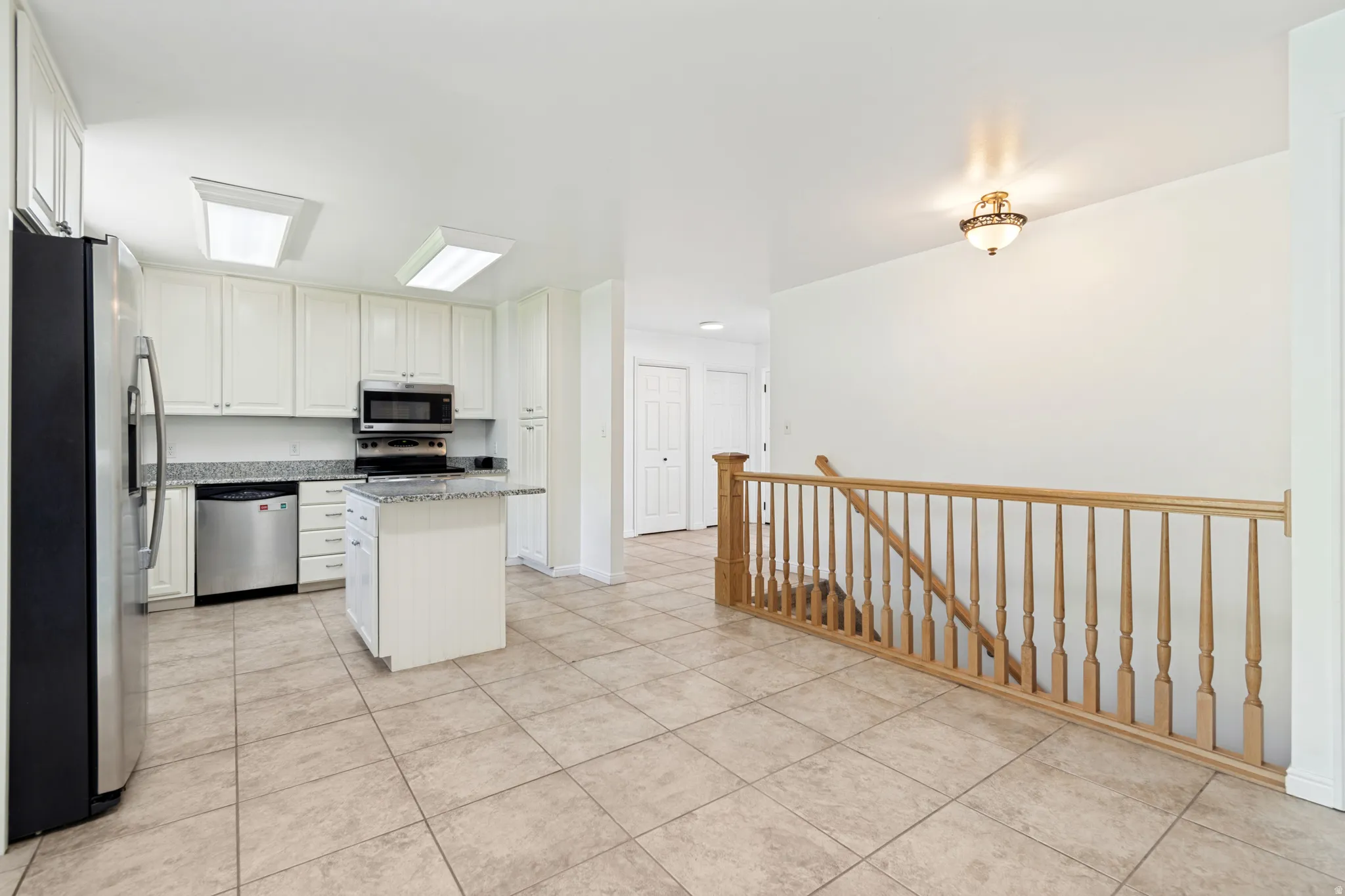 Kitchen featuring white cabinetry, stainless steel appliances, a center island with a granite-style countertop, and neutral tile flooring