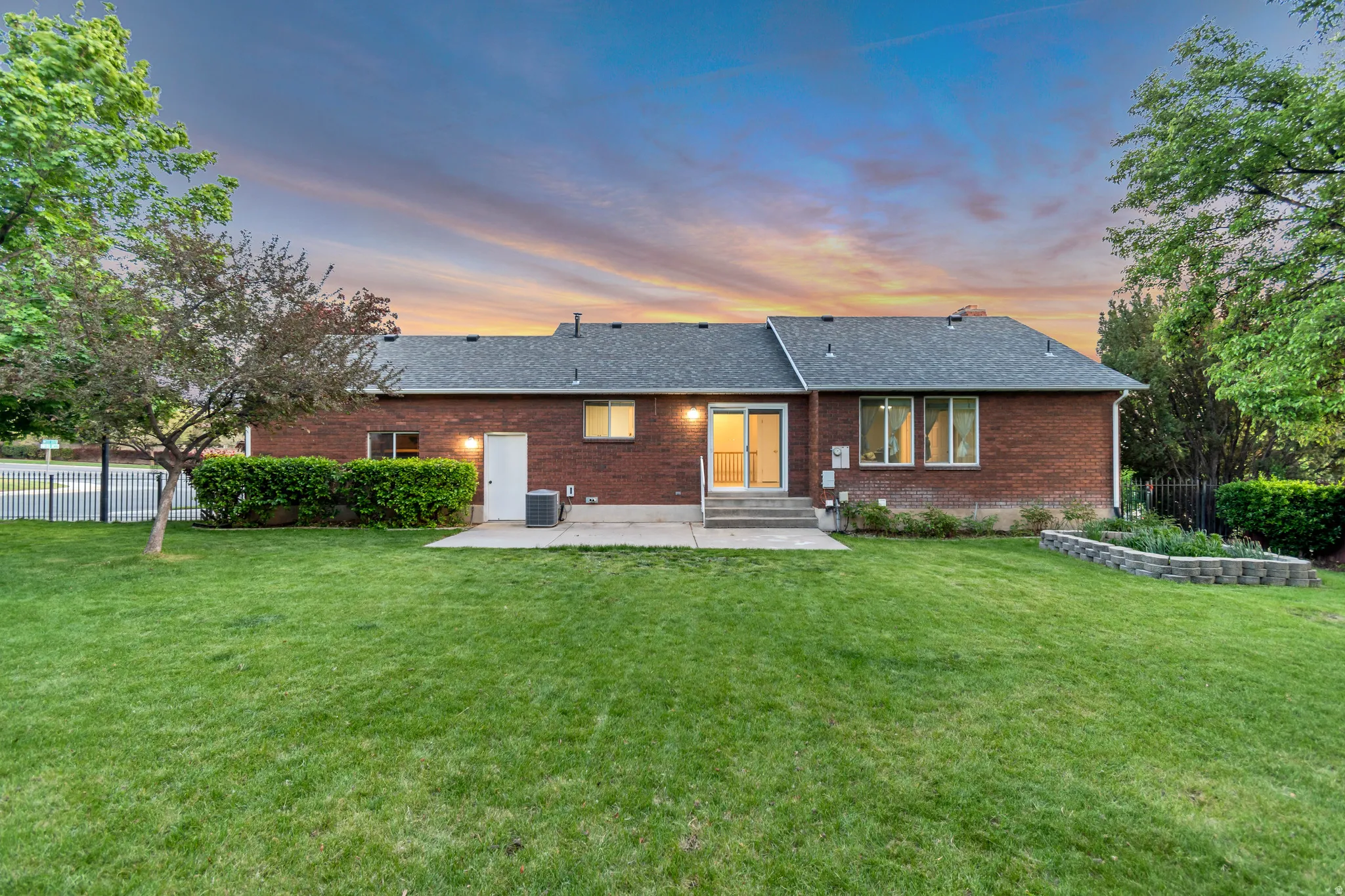 Expansive green lawn with a brick exterior, mature trees, and a raised garden bed