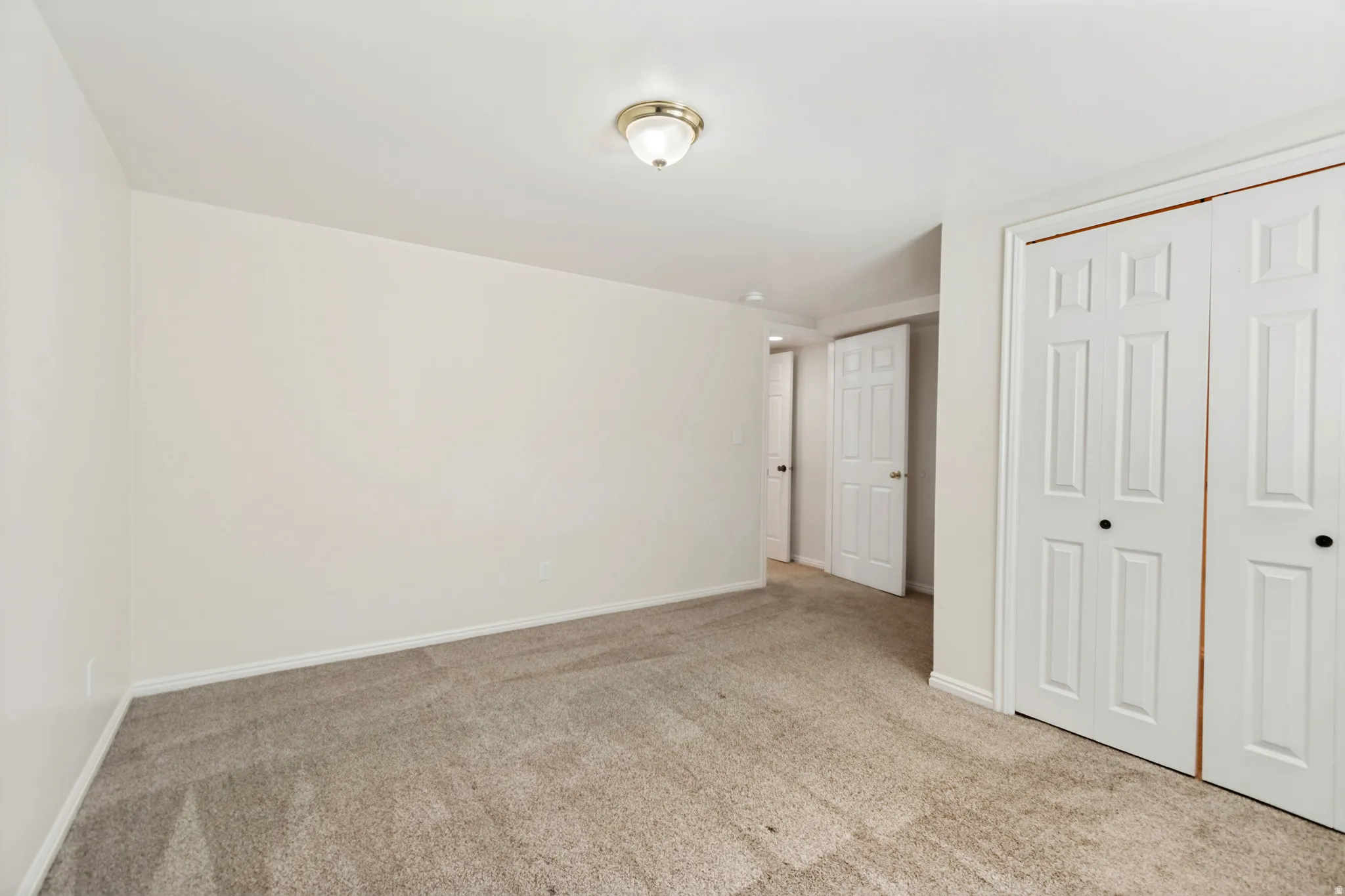 Spacious room featuring neutral carpeting, light-colored walls, white baseboards, and a flush-mount ceiling light fixture