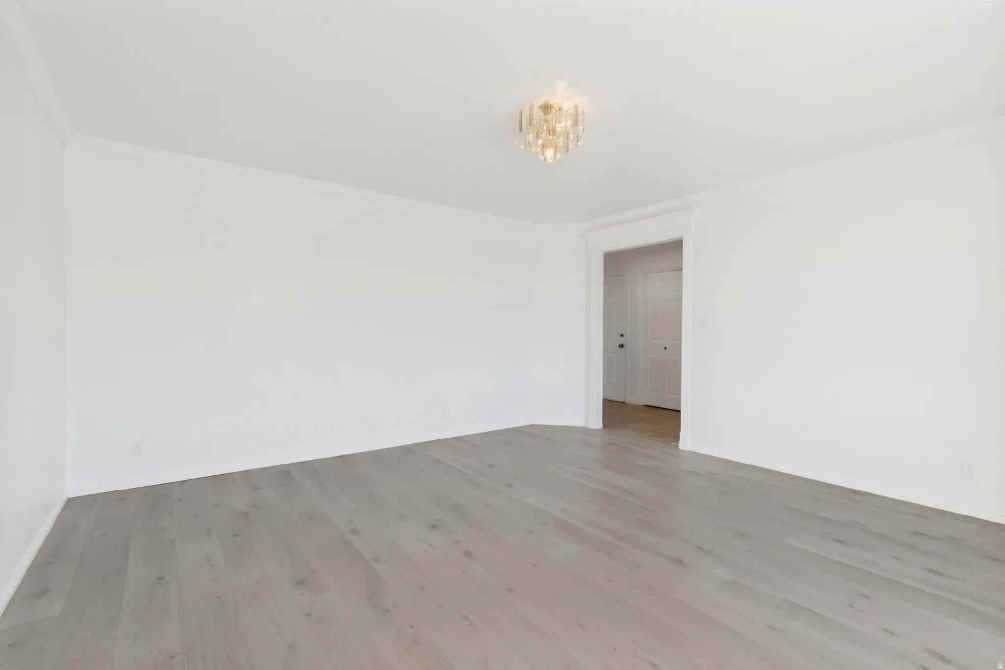 Spacious room featuring light wood-finish flooring, white walls, and a contemporary crystal chandelier