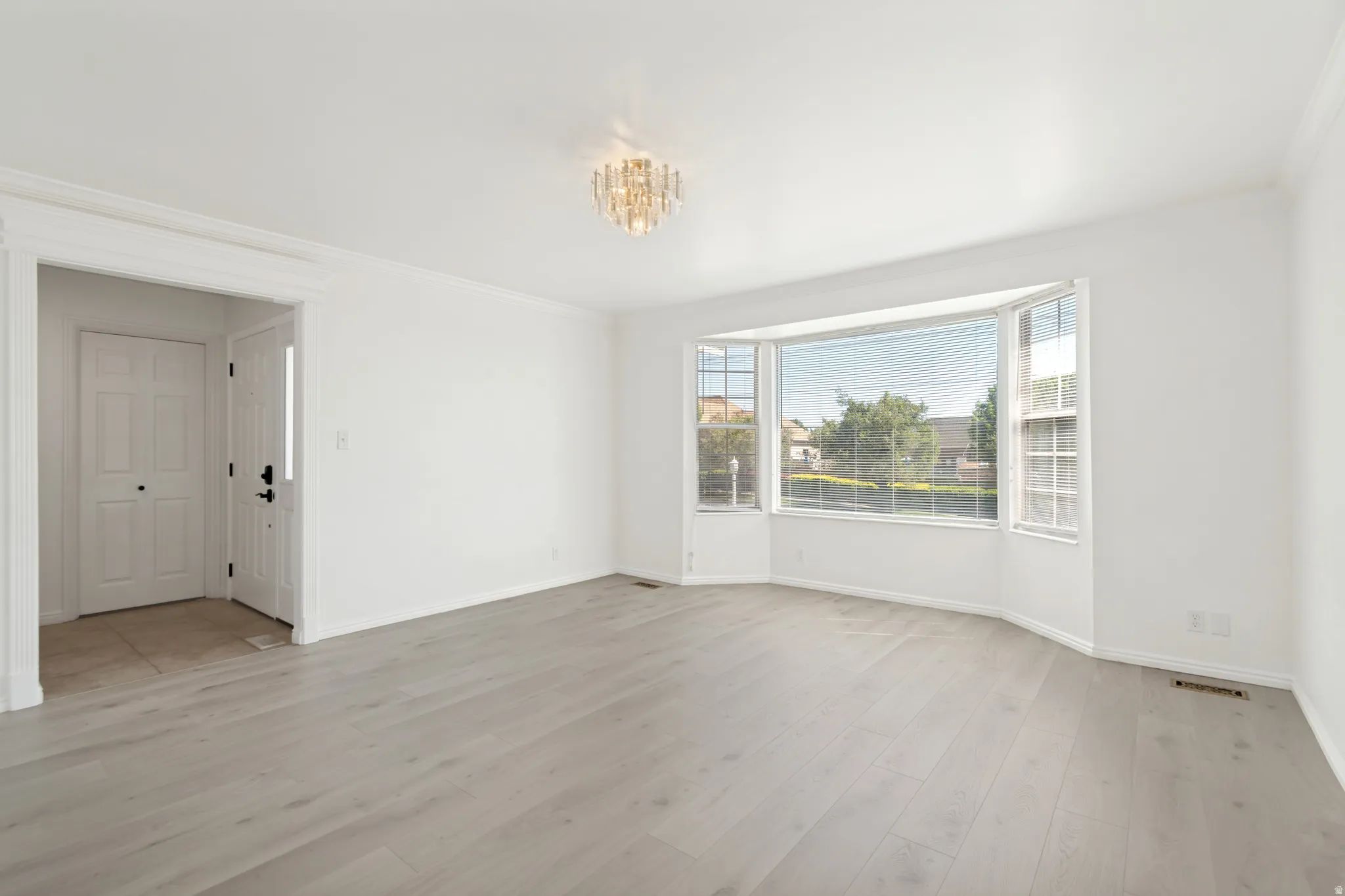 Spacious interior room featuring a prominent bay window, light wood-finish flooring, white walls, and elegant crown molding