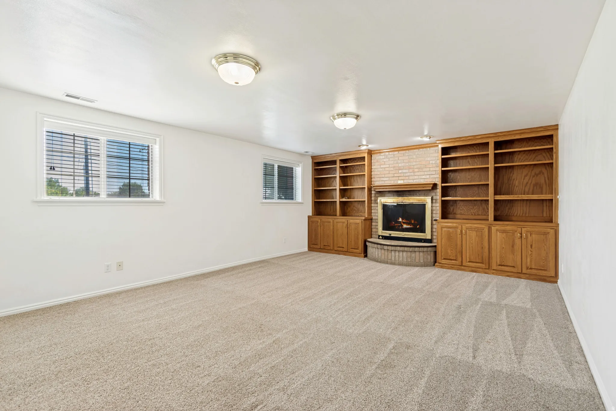 Spacious room featuring extensive built-in wood cabinetry and shelving, a brick-surround fireplace, and two windows with blinds