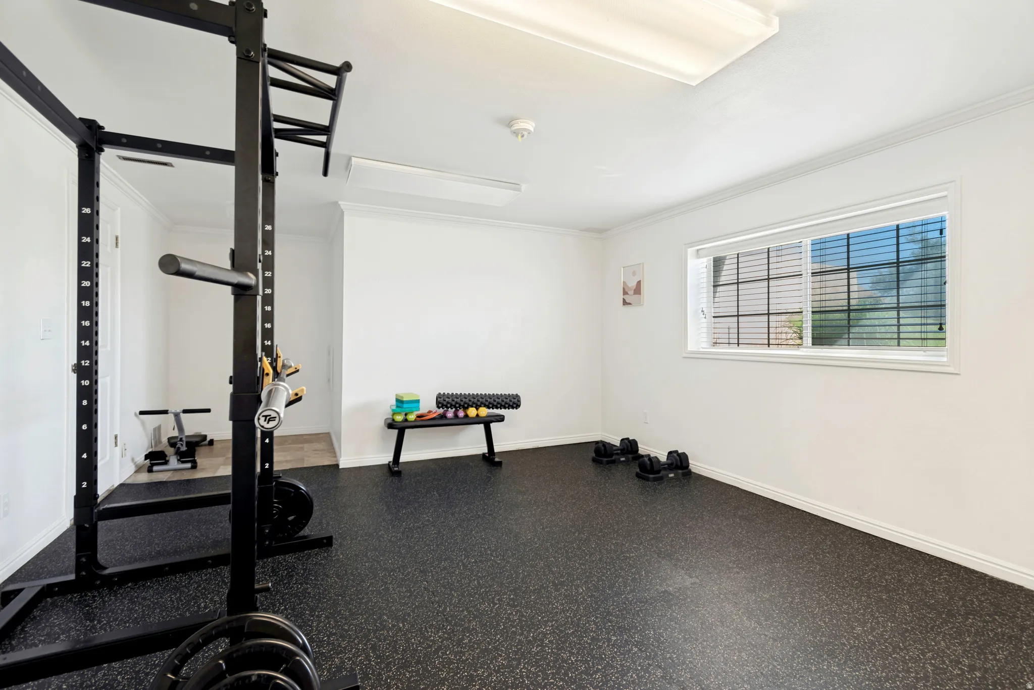 Flexible-use room featuring durable rubber flooring, white baseboards, and a large window with horizontal blinds