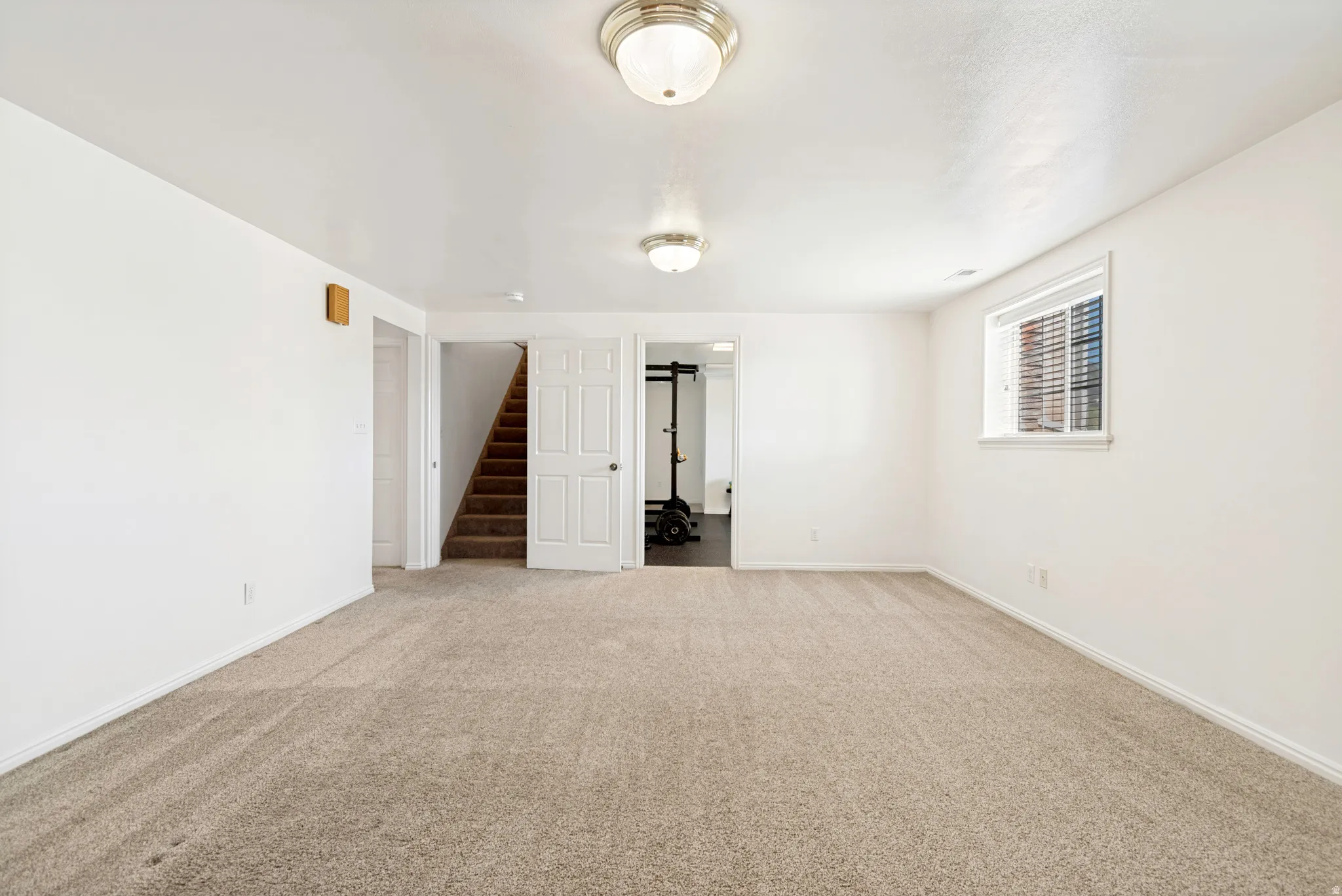 Spacious room featuring neutral carpeting, white walls, and a window with blinds