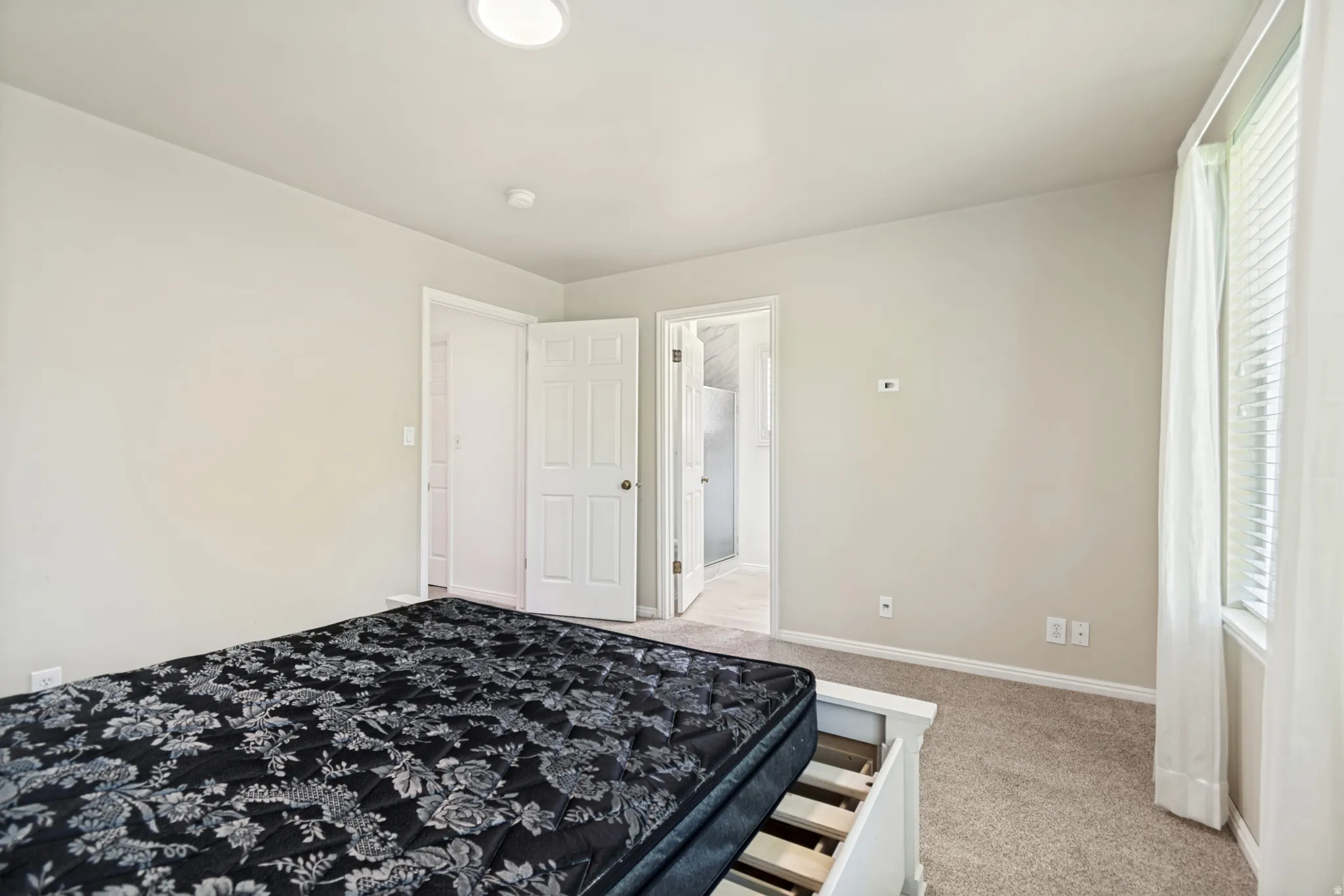 Carpeted room featuring a ceiling-mounted light fixture, white trim, and a window with blinds