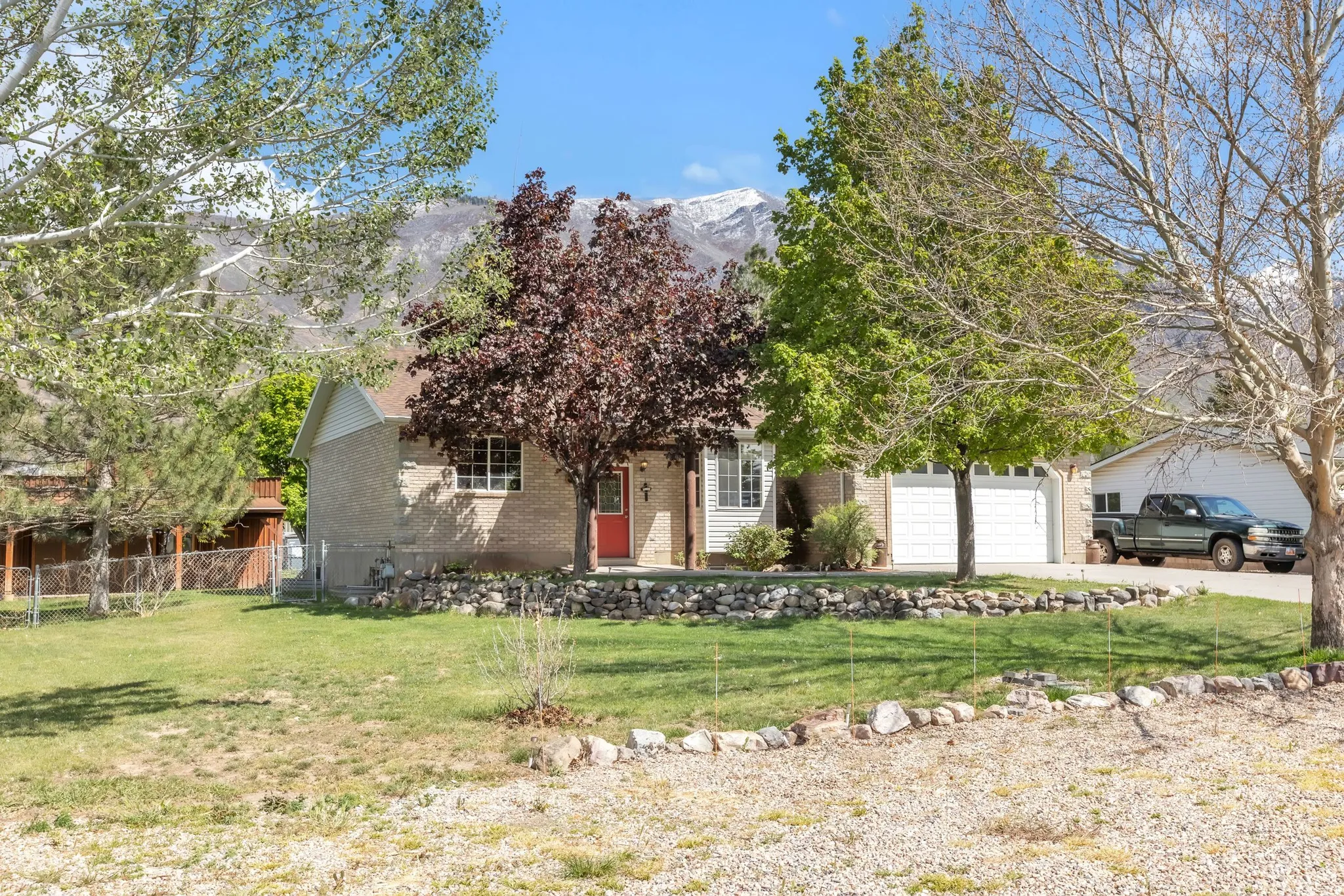 View of property hidden behind natural elements featuring brick siding, a mountain view, concrete driveway, and an attached garage